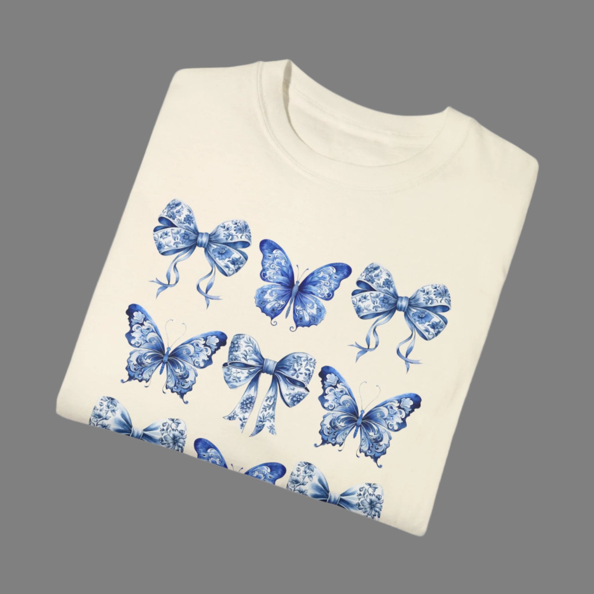 Image: This women’s tee showcases a romantic blue toile pattern filled with fluttering butterflies and dainty bows, tailored for fans of the soft girl and bougie mama aesthetic. Inspired by French toile de jouy and reimagined with a coastal cowgirl twist, it’s a versatile piece made for everyday wear or matching family looks. Coordinates with toddler and youth options for unforgettable photos, by jaecrece.