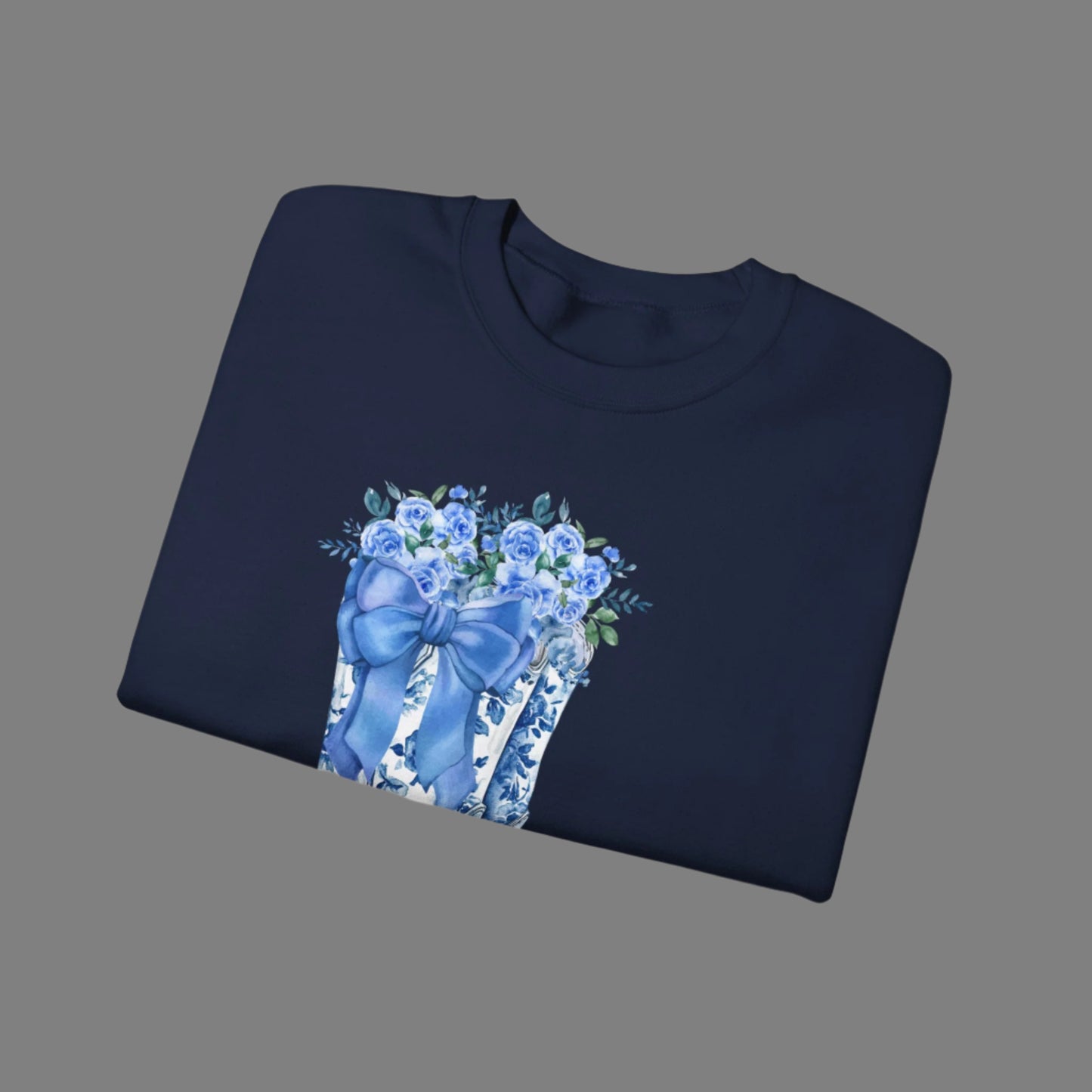 Image: This cozy women's sweatshirt features a stunning blue toile design with cowboy boots, a bow, and delicate wildflowers, capturing the essence of a soft western aesthetic. The relaxed fit and breathable fabric make it a must-have for country lovers who appreciate timeless fashion. Whether worn at a rodeo, a fall festival, or simply as a stylish everyday piece, this pullover is a thoughtful gift for daughters, moms, or cowgirls at heart, by jaecrece.