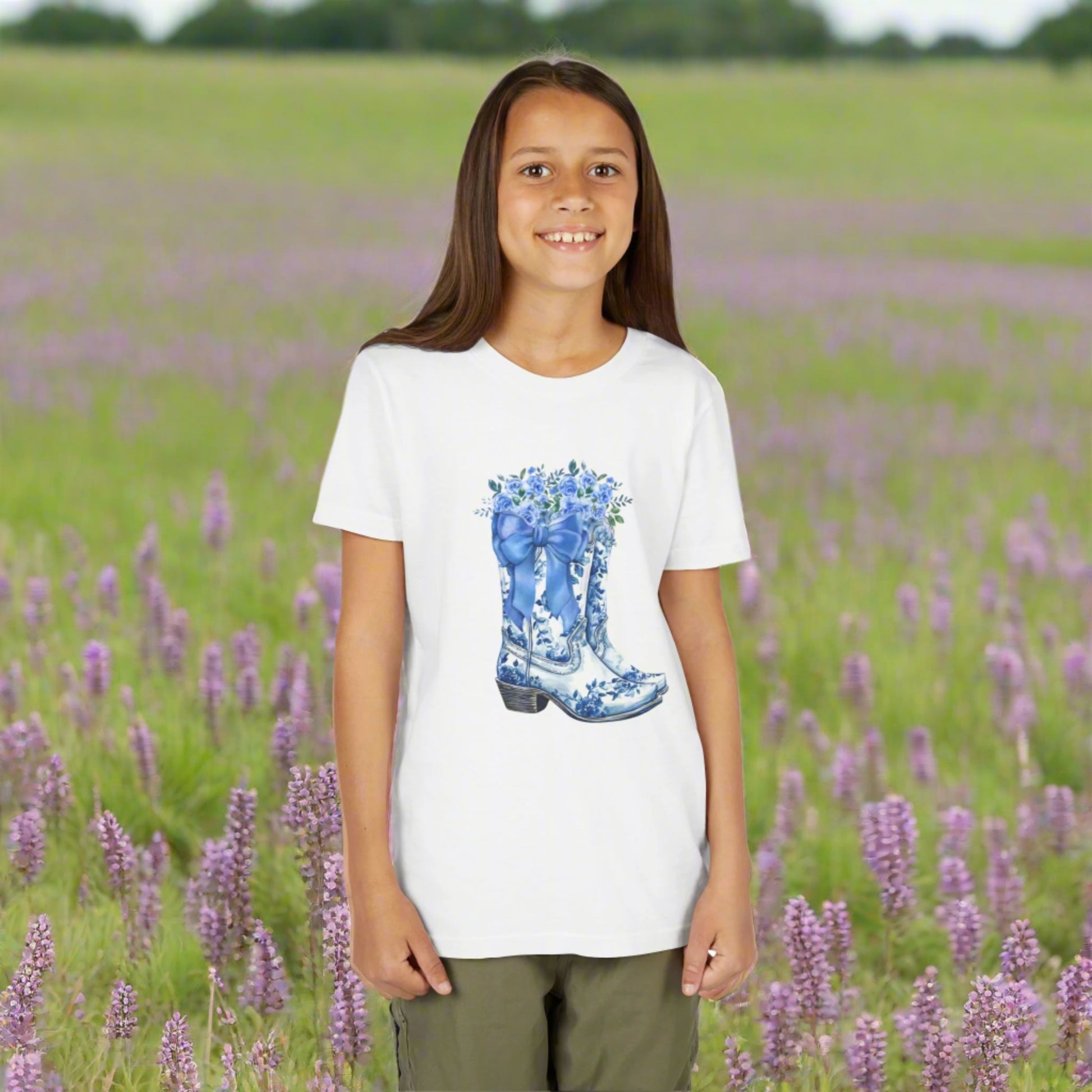 Image: A stylish gift for girls who love a little country sparkle, this youth shirt features a blue bow, wildflowers, and a pair of classic western boots. The light blue toile design adds elegance to a playful cowgirl look. Available in girls sizes S to XL, this soft tee is perfect for casual days, cool weather adventures, or family outings with southern flair, by jaecrece.