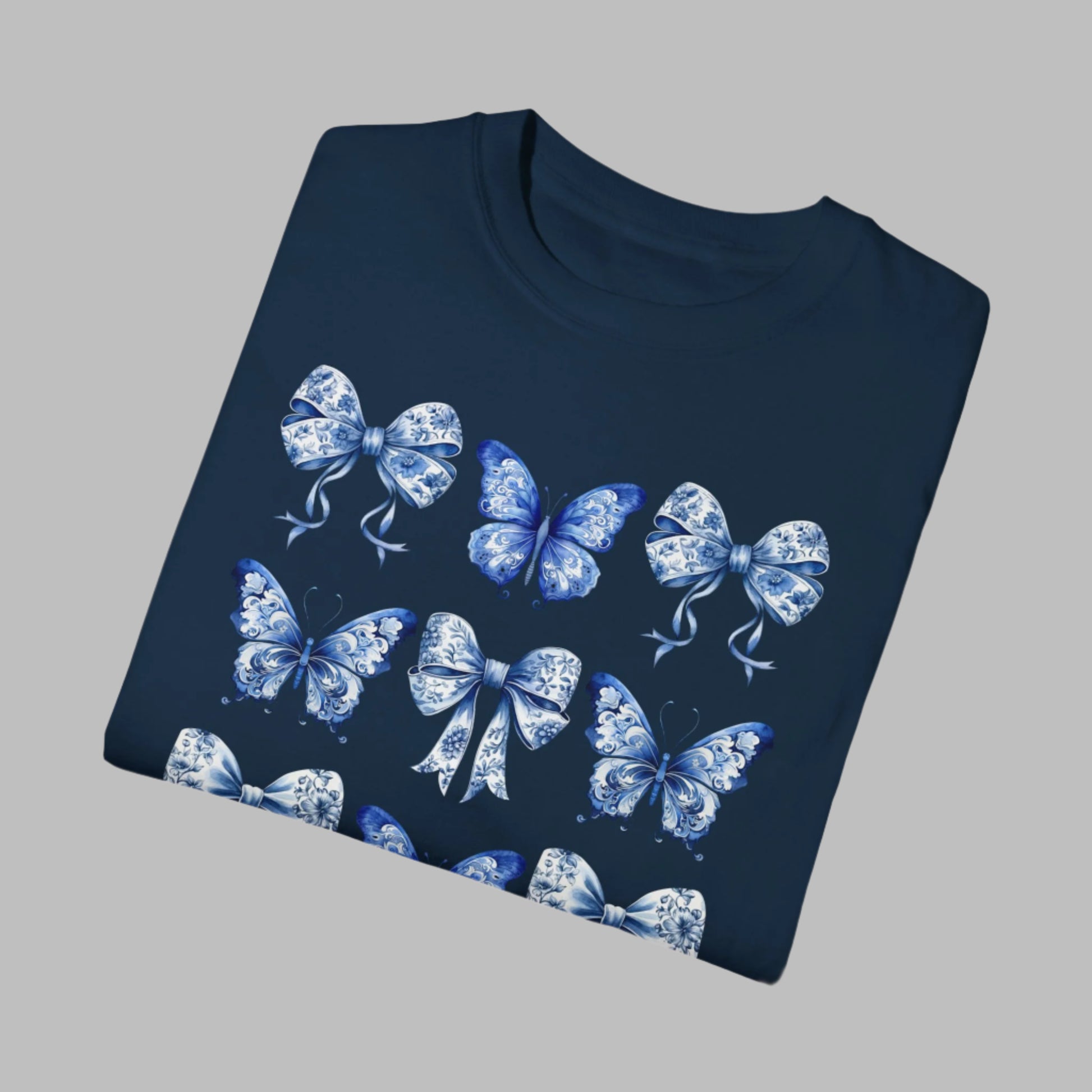 Image: With its dreamy butterfly and bow motif set against a vintage-inspired blue toile background, this women’s shirt blends soft girl style with French country elegance. A staple for bougie mamas and fans of the chinoiserie trend, it’s the perfect tee for family gatherings or spring strolls. Match it with girls’ and toddler sizes for an Instagram-ready mother-daughter look, by jaecrece.