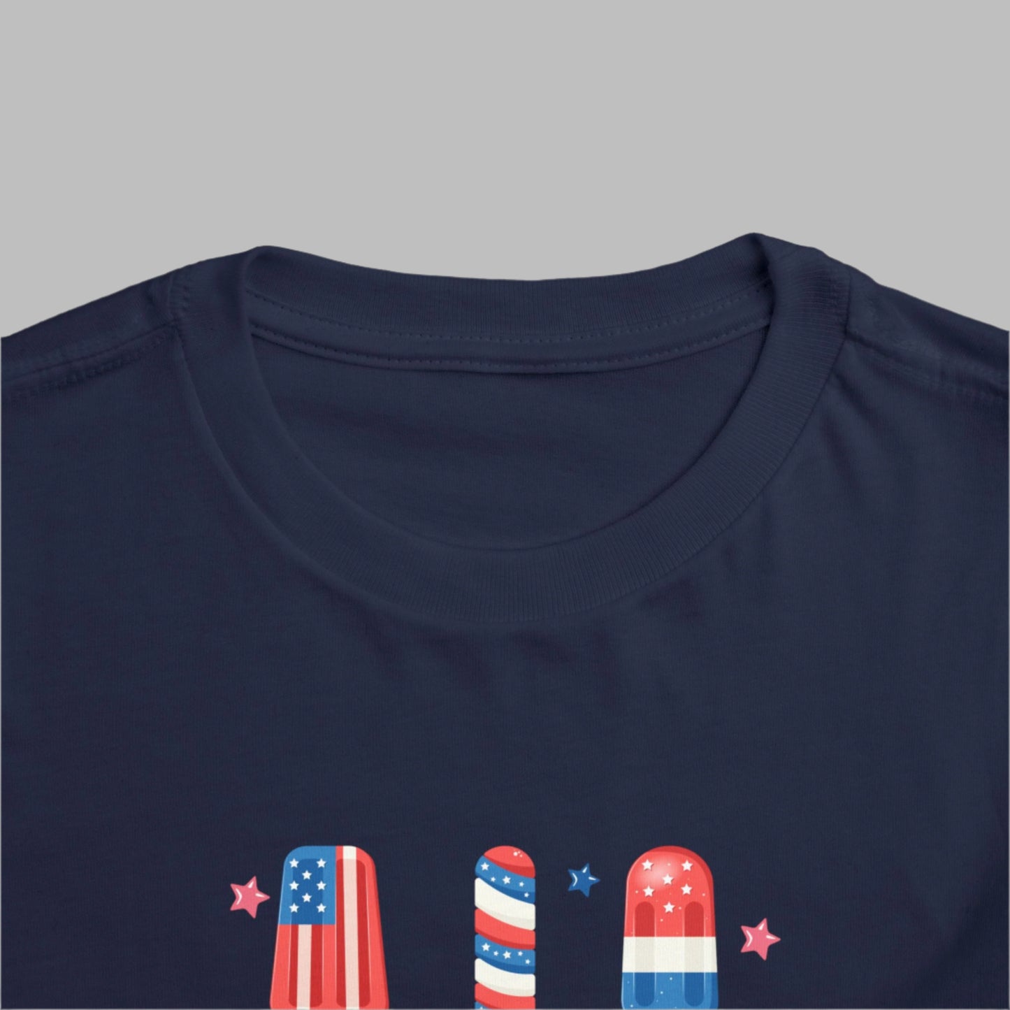 Image: Toddler size Independence Day shirt featuring a bright patriotic popsicle design in red white and blue. A cute and cozy summer outfit for Memorial Day fun or 4th of July fireworks. Perfect for toddlers who want to match with family in style, this tee is ideal for a day of celebration, snacks, and American pride under the sun, by jaecrece.
