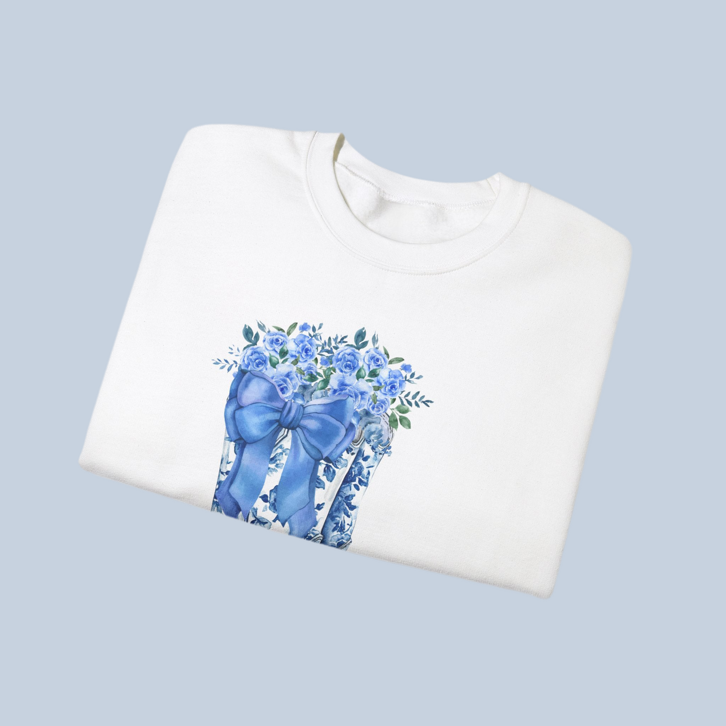 Image: This cozy women's sweatshirt features a stunning blue toile design with cowboy boots, a bow, and delicate wildflowers, capturing the essence of a soft western aesthetic. The relaxed fit and breathable fabric make it a must-have for country lovers who appreciate timeless fashion. Whether worn at a rodeo, a fall festival, or simply as a stylish everyday piece, this pullover is a thoughtful gift for daughters, moms, or cowgirls at heart, by jaecrece.