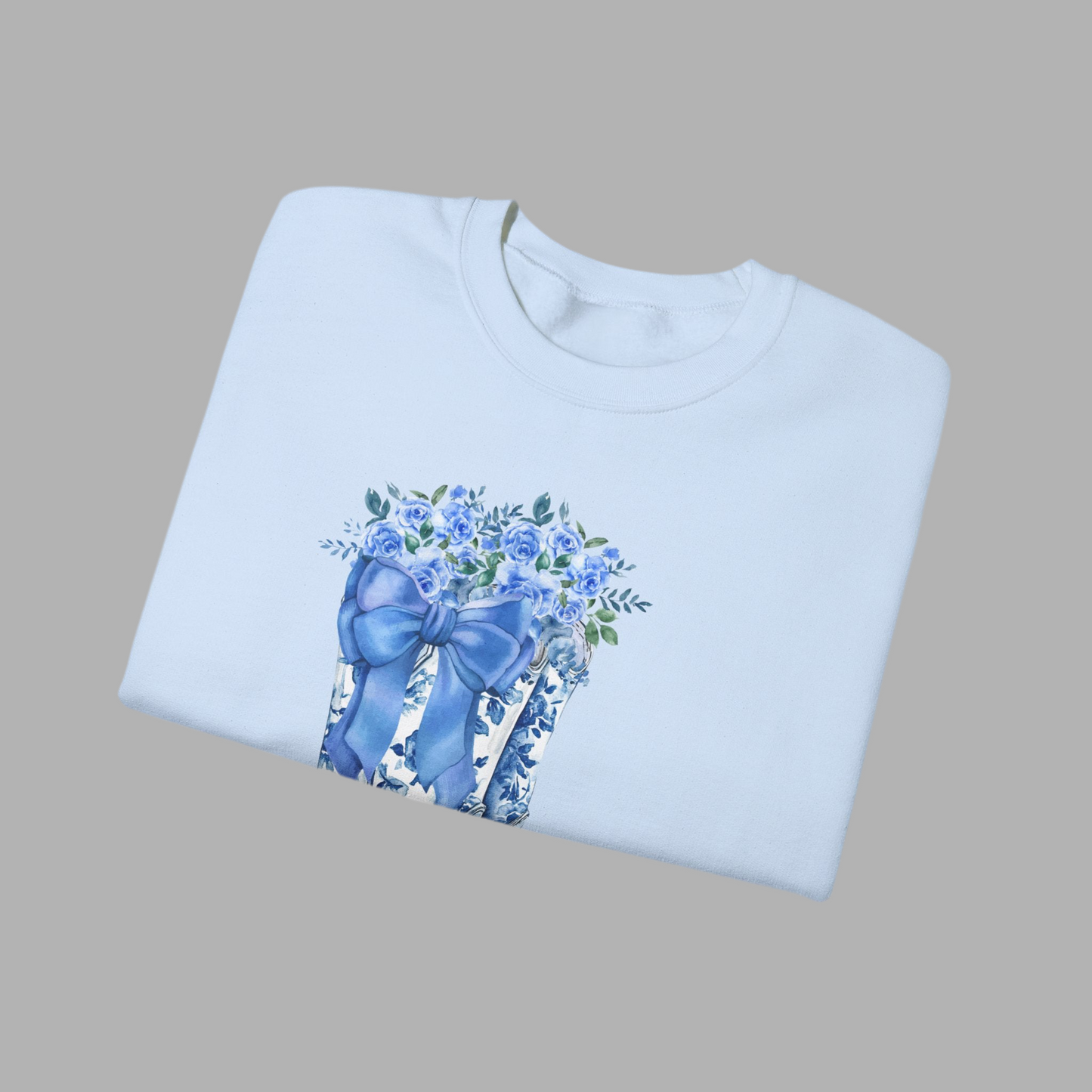 Image: This cozy women's sweatshirt features a stunning blue toile design with cowboy boots, a bow, and delicate wildflowers, capturing the essence of a soft western aesthetic. The relaxed fit and breathable fabric make it a must-have for country lovers who appreciate timeless fashion. Whether worn at a rodeo, a fall festival, or simply as a stylish everyday piece, this pullover is a thoughtful gift for daughters, moms, or cowgirls at heart, by jaecrece.