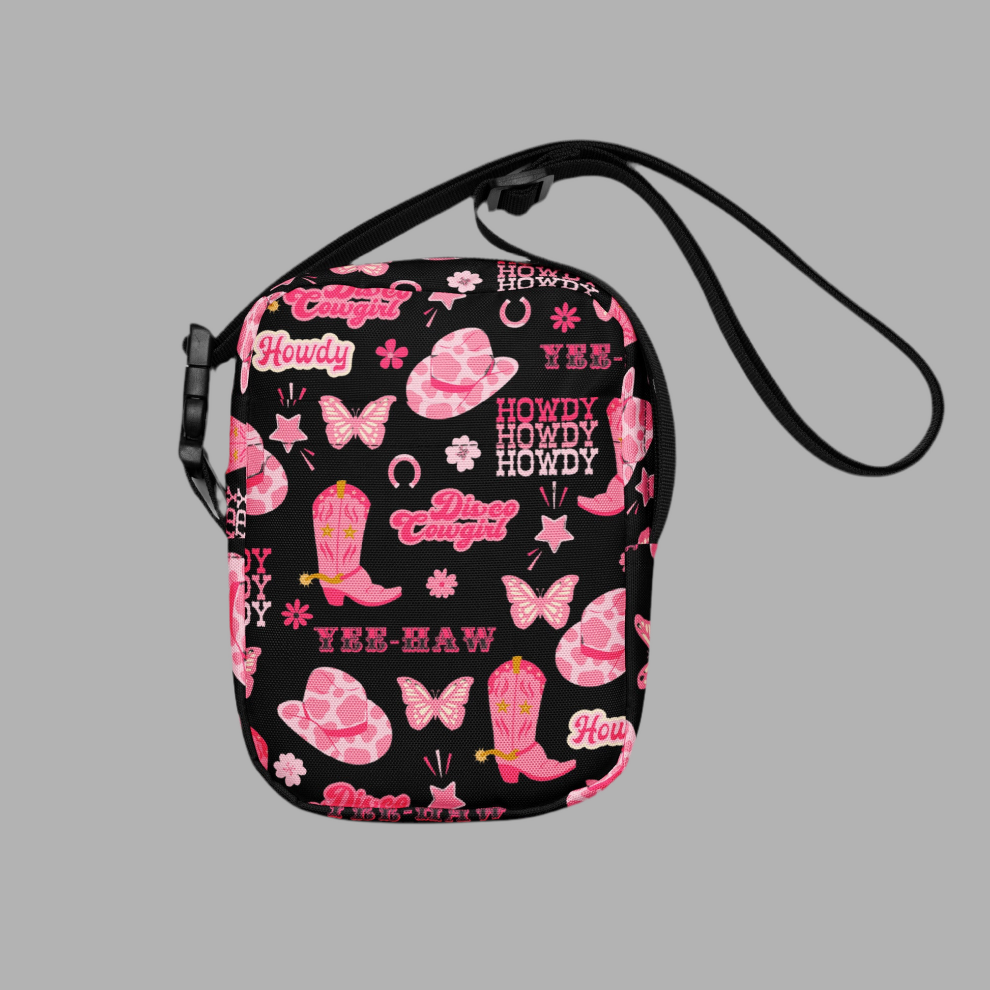 Image: Disco Cowgirl Canvas Crossbody Bag. This small black sling bag features a western glam hot pink pattern of cowgirl boots, cowgirl hats, butterflies and horseshoes. The pattern reads Disco Cowgirl, Yee-Haw and Howdy. The perfect mini backpack for bachelorette parties, gifts for teens or tweens, or trips to the state fair, by jaecrece