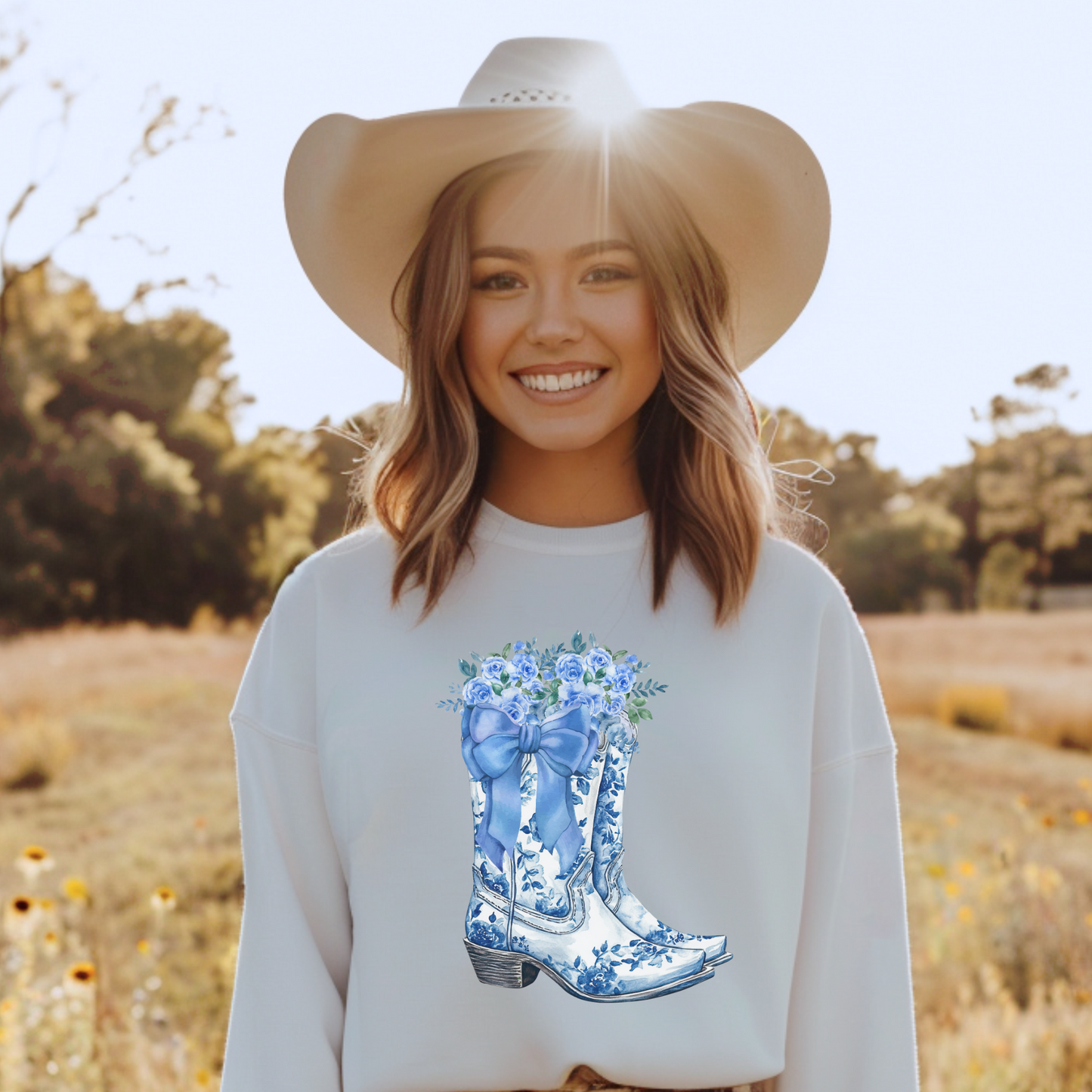 Image: A beautifully designed women's sweatshirt featuring a charming blue toile print of cowboy boots, a bow, and wildflowers. This soft and stylish pullover brings together country elegance and casual comfort, making it ideal for layering on cool days. Whether you are a rodeo queen, a farmhouse fashion lover, or simply adore western aesthetics, this sweatshirt makes the perfect gift for moms, daughters, or anyone embracing the cowgirl spirit, by jaecrece.