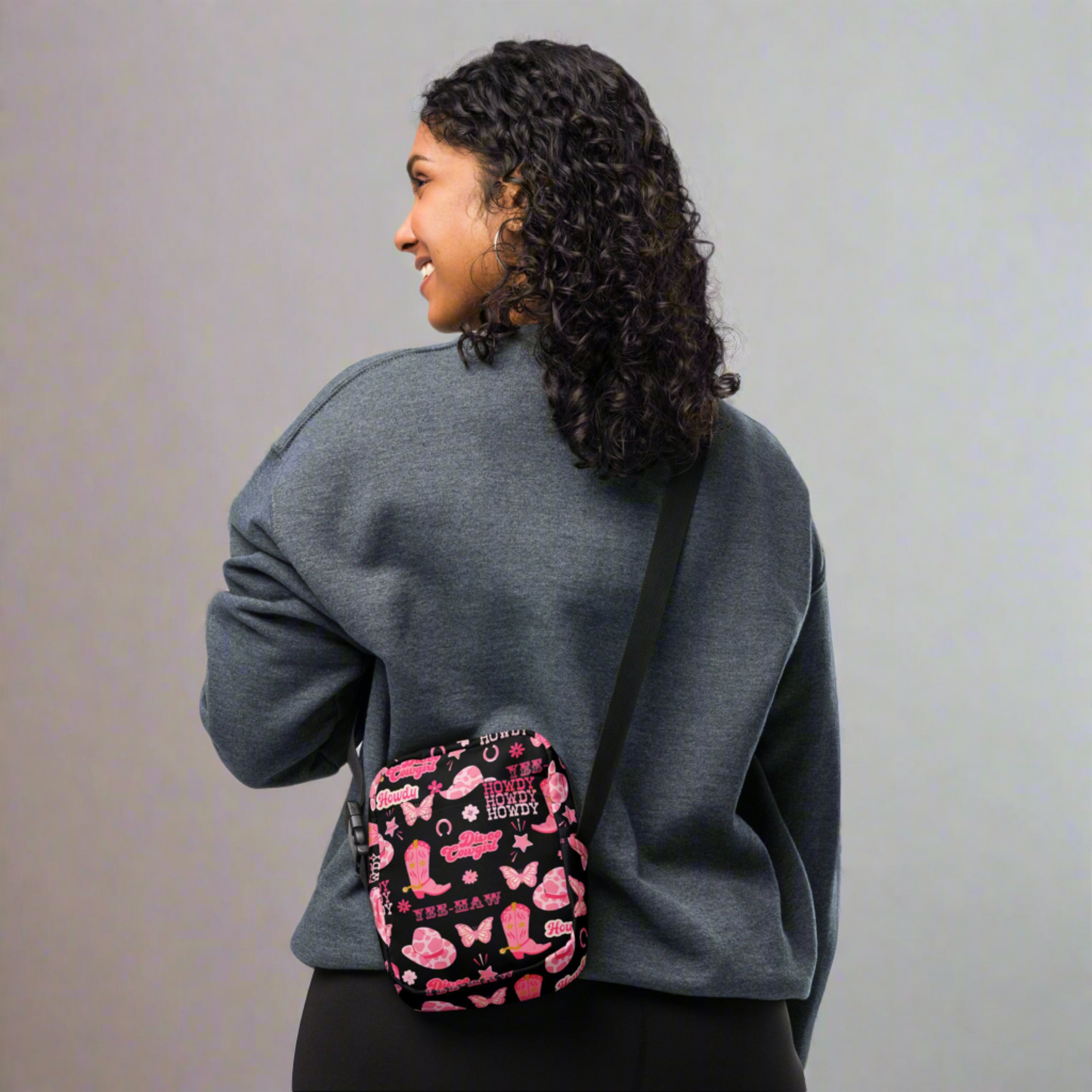 Image: Disco Cowgirl Canvas Crossbody Bag. This small black sling bag features a western glam hot pink pattern of cowgirl boots, cowgirl hats, butterflies and horseshoes. The pattern reads Disco Cowgirl, Yee-Haw and Howdy. The perfect mini backpack for bachelorette parties, gifts for teens or tweens, or trips to the state fair, by jaecrece