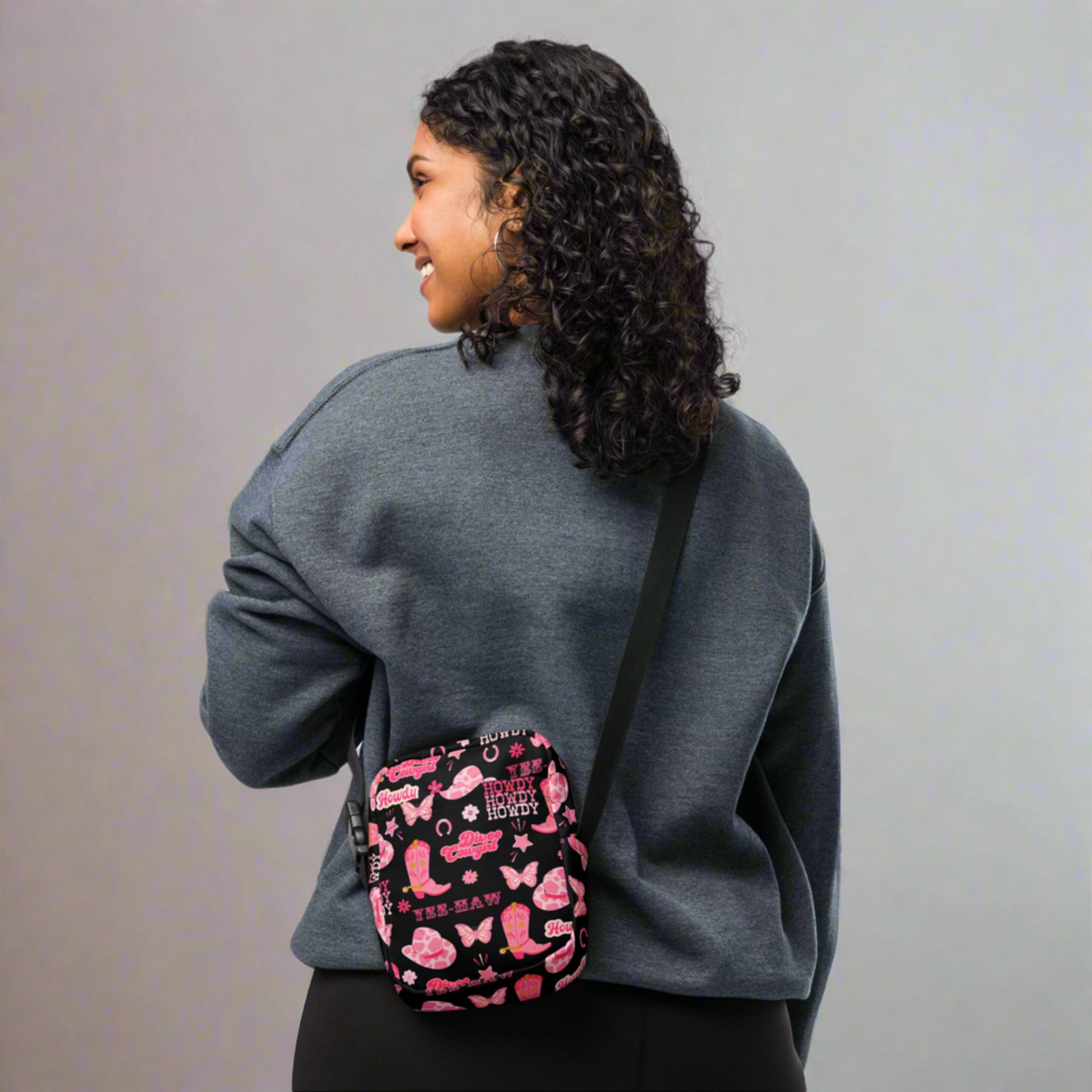 Image: Disco Cowgirl Canvas Crossbody Bag. This small black sling bag features a western glam hot pink pattern of cowgirl boots, cowgirl hats, butterflies and horseshoes. The pattern reads Disco Cowgirl, Yee-Haw and Howdy. The perfect mini backpack for bachelorette parties, gifts for teens or tweens, or trips to the state fair, by jaecrece