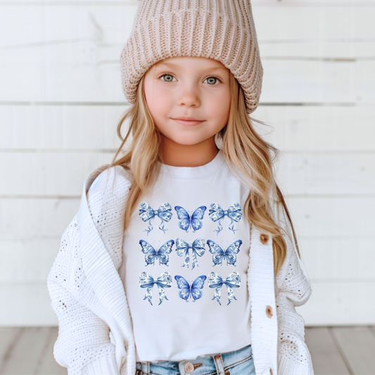 Blue Toile Toddler T-shirt for girls features a delicate pattern of bows and butterflies, inspired by the Texas coquette trend and coastal cowgirl fashion. Designed in calming shades of blue on a soft white background, this spring and summer shirt brings elegance and comfort to your child’s wardrobe. A perfect outfit choice for birthdays, beach trips, or family photos. Available in toddler sizes 2T through 7 for stylish little girls, by jaecrece.