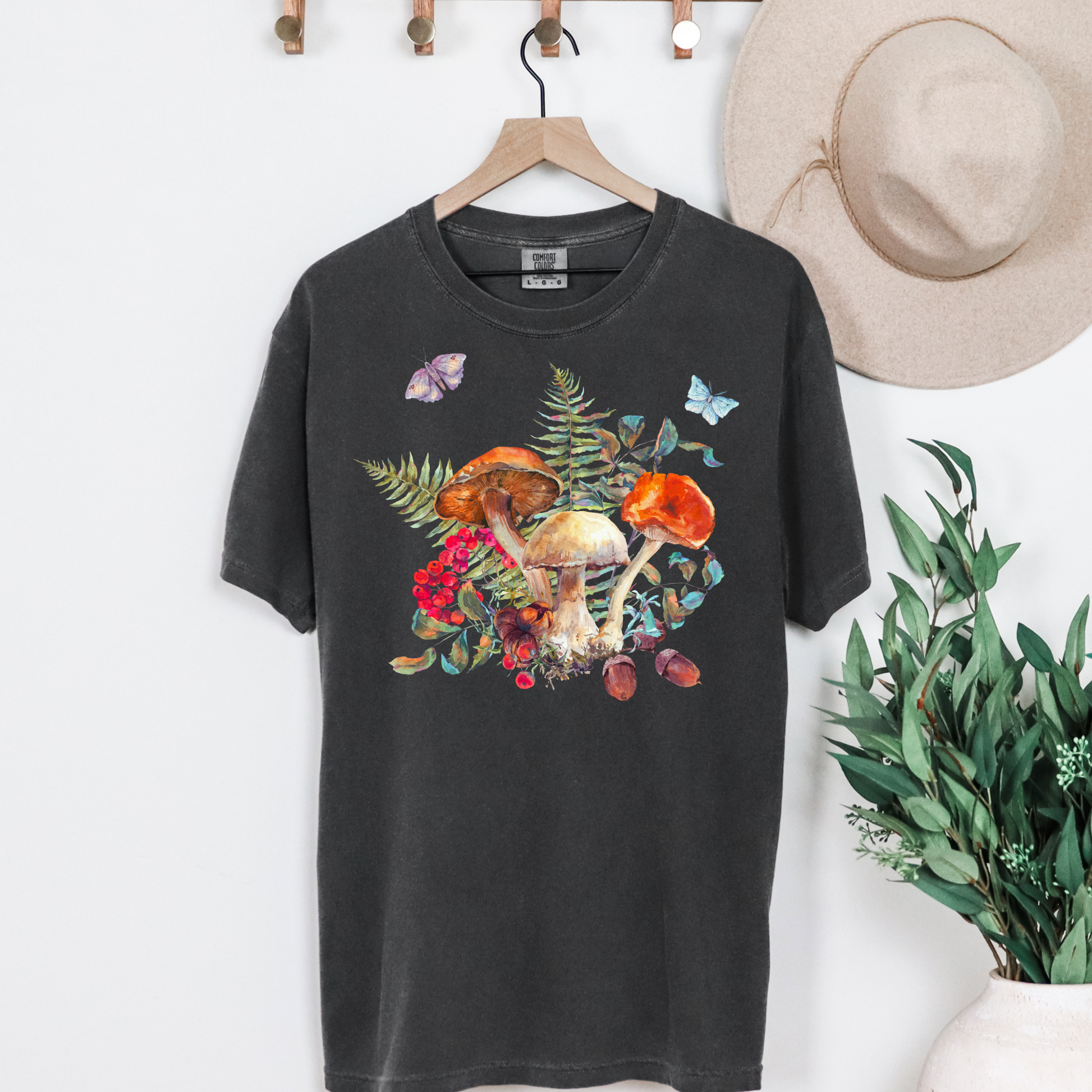 Whimsical Boho Botanical Mushroom Shirt on Comfort Colors 1717 tee with oversized garden-inspired mushrooms, ferns, butterflies, and moths. Available in earthy tones Ivory, Blue Spruce, Butter, Granite, and Pepper, this unisex woodland graphic shirt fits perfectly into cottagecore, goblincore, fairyboho, and boho mystic fashion trends. Soft and relaxed for fall layering or casual autumn wear, this made-to-order botanical tee is eco-conscious and a perfect gift for mushroom lovers, forest enthusiasts, plant