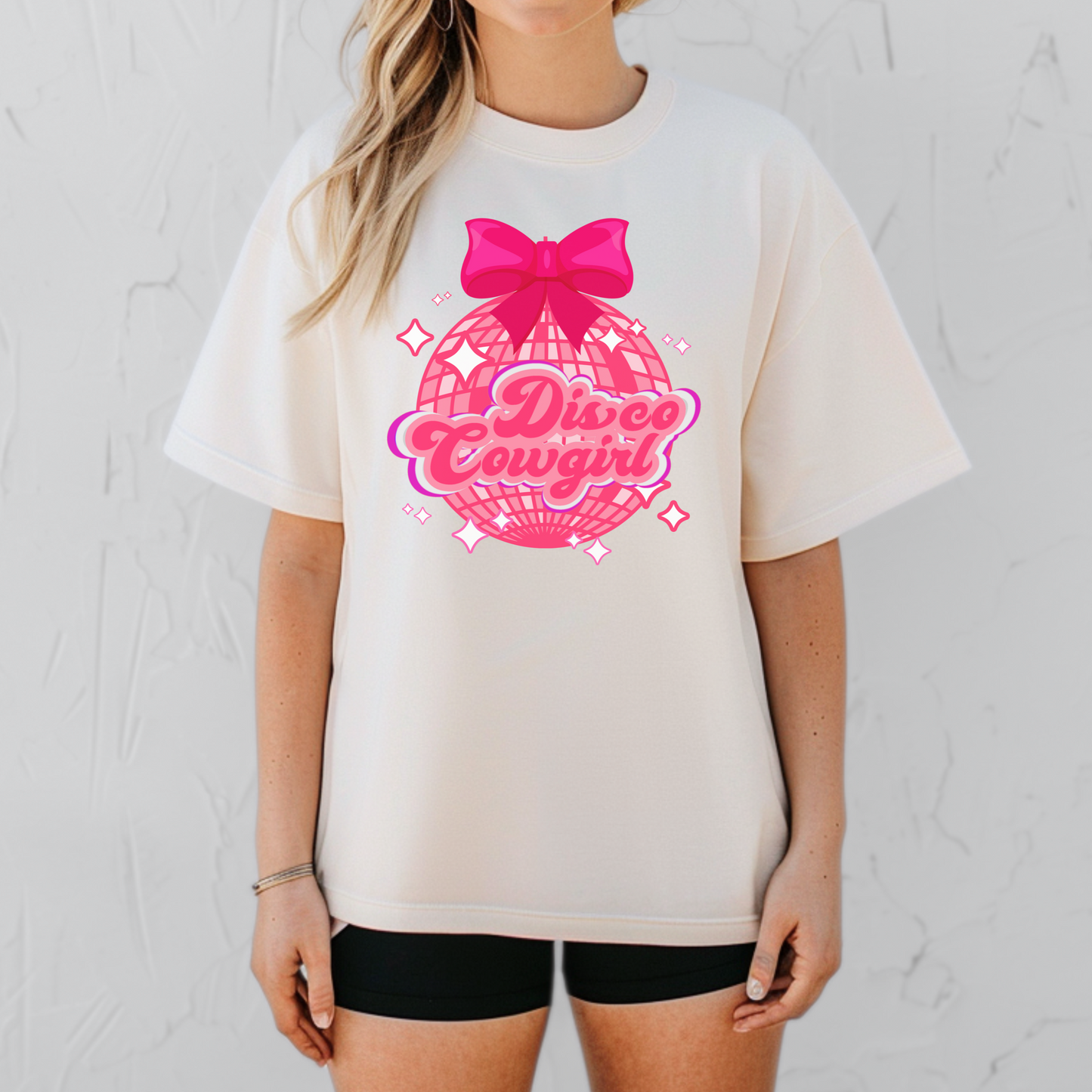 This Comfort Colors Disco Cowgirl shirt for women features a sparkly pink disco ball, bold pink and purple lettering, and a coquette hot pink bow. A fun western-themed t-shirt perfect for bachelorette parties, rodeo season, country concerts, and girls’ trips. The relaxed, vintage fit makes this a festival-ready favorite. Available in black, ivory, white, and pepper, sizes S–4XL.