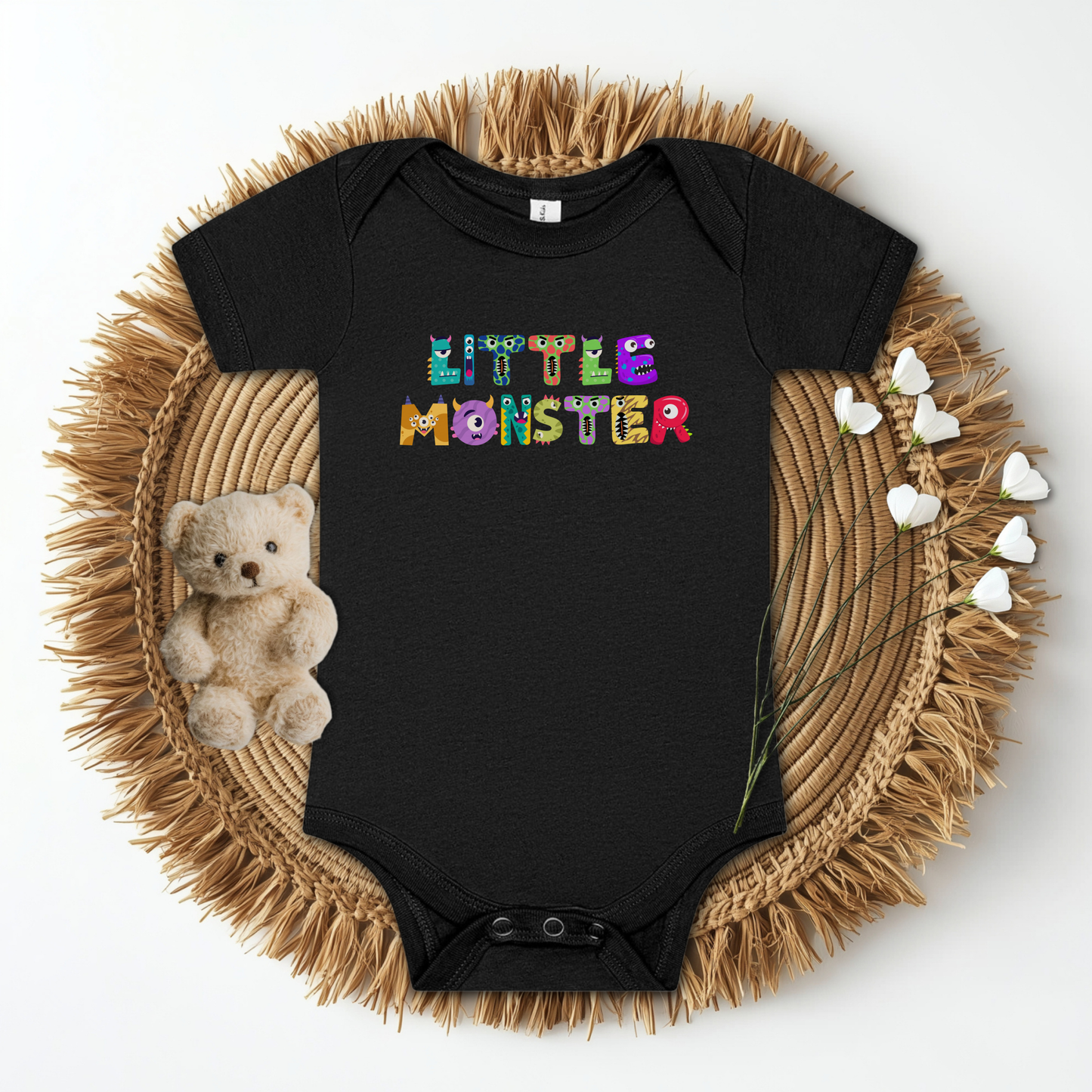 Flat lay of the black Little Monster baby bodysuit, featuring playful cartoon monster letters spelling “little monster” across the chest. Printed on a Bella + Canvas 100B infant one-piece, this soft cotton bodysuit is lightweight, breathable, and gentle on baby’s skin. Designed with an envelope neckline and snap closure for easy changes, it makes the perfect first Halloween outfit, fall romper, or baby shower gift. Available newborn through 24 months.