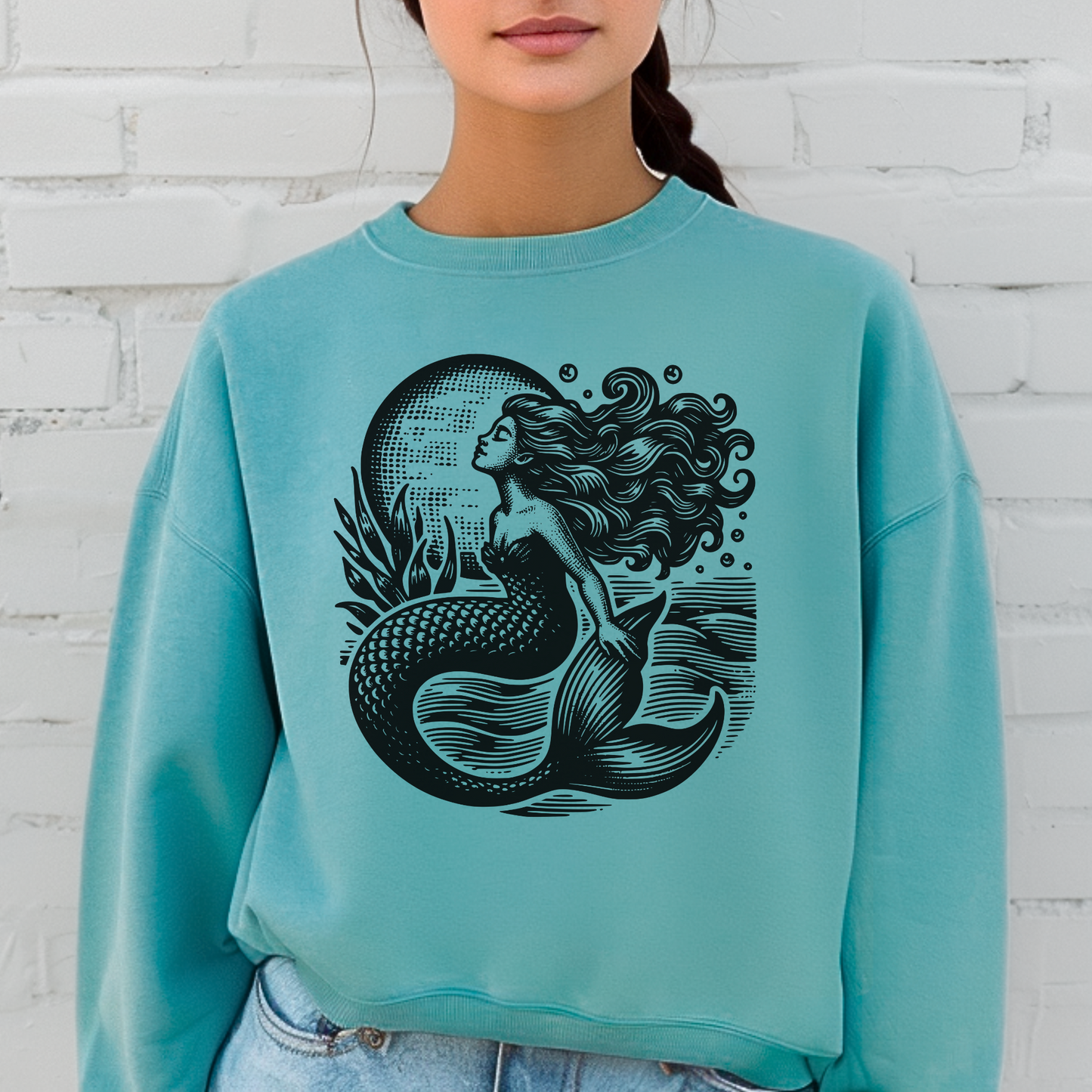 Woman wearing a Comfort Colors 1566 sweatshirt in Seafoam green featuring a vintage mermaid graphic with flowing hair, scales, and sea-inspired details. This cozy pullover blends coastal aesthetic charm with cottagecore whimsy, perfect for women who love ocean fashion, fantasy art, and relaxed everyday style. Made from a soft cotton blend with a loose, comfortable fit, it’s a versatile piece for casual outings, layering, or gifting to beach lovers and nautical style fans.