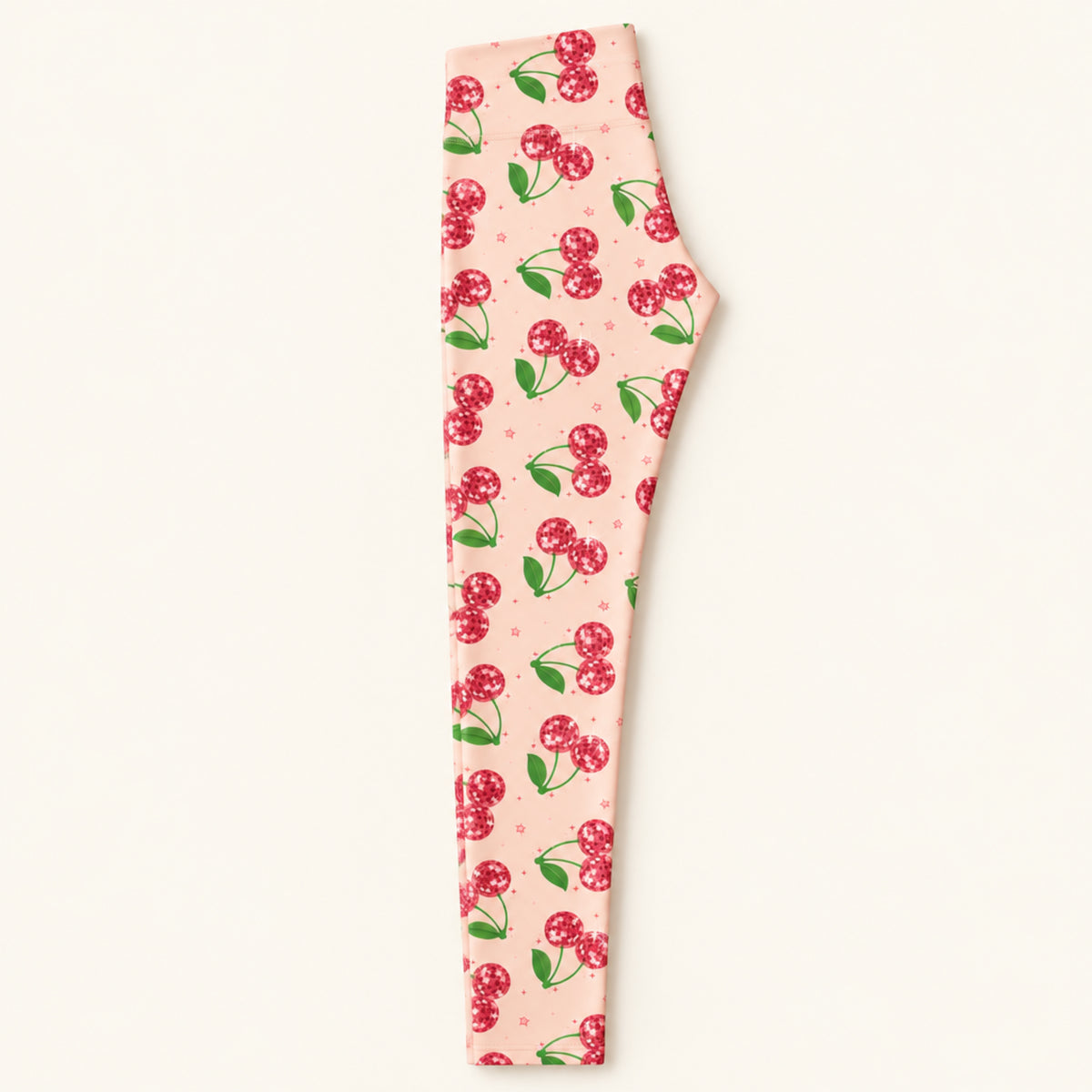 Long folded view of pink cherry print womens leggings showing the bright pink fabric, sparkling red cherry design and full length silhouette. The neatly folded mid rise leggings highlight the colorful retro fruit print and smooth fabric while giving shoppers a clear view of the overall garment and design.