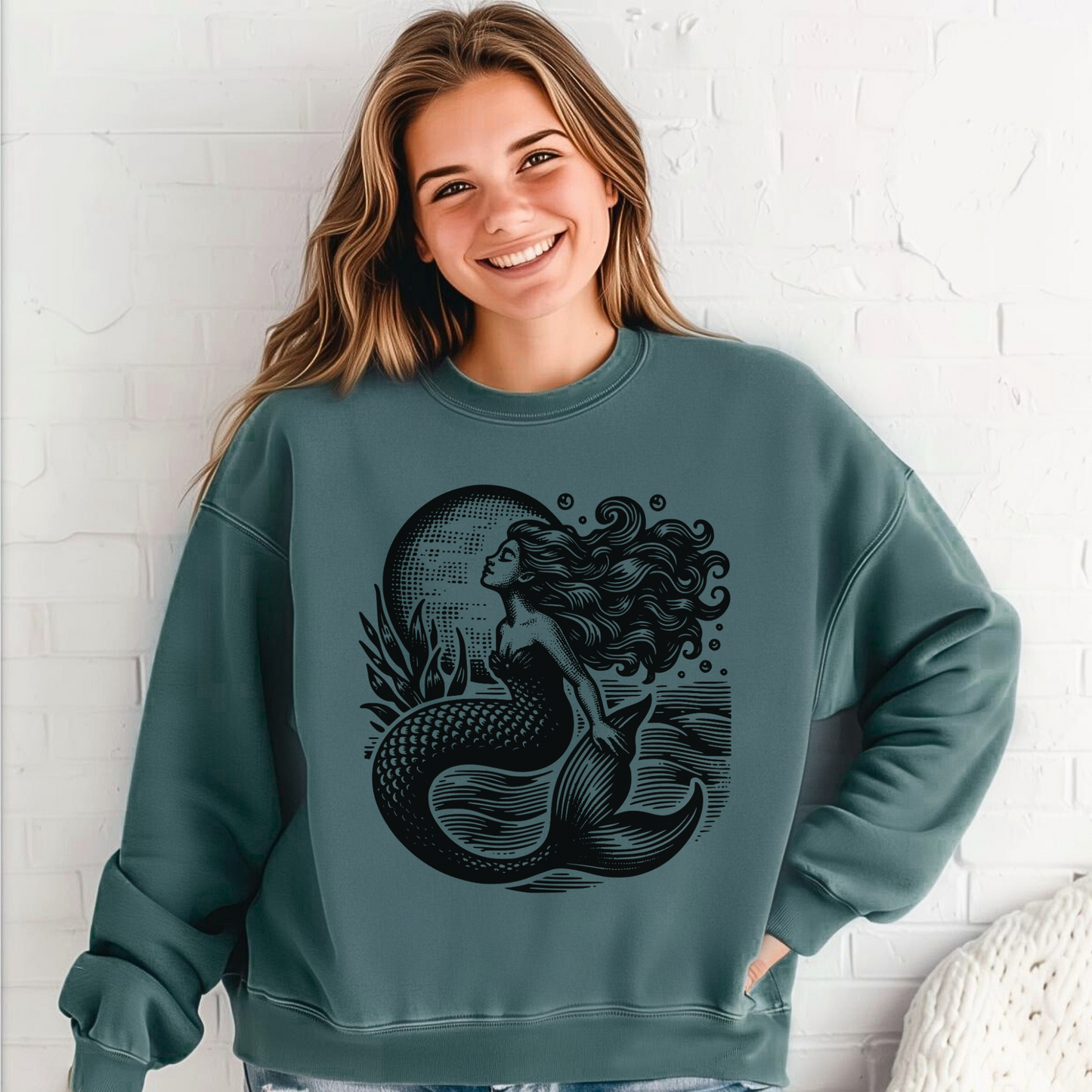 Teen girl wearing a Comfort Colors 1566 sweatshirt in Blue Spruce featuring a detailed vintage mermaid graphic. The ocean-inspired design shows a graceful mermaid with flowing hair, scales, and sea plants against a moonlit backdrop, giving it a nautical and fantasy feel. This cozy cotton blend pullover has a relaxed fit, making it perfect for women and teens who love coastal fashion, mermaid art, and whimsical ocean-themed clothing.