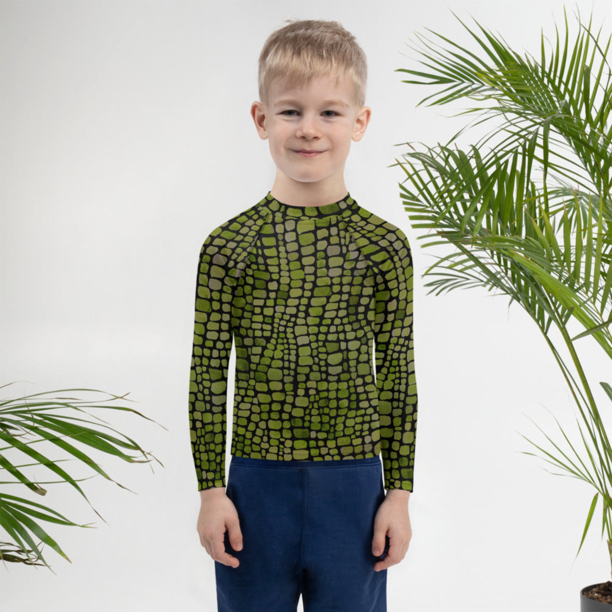 Green reptile rash guard for toddlers and kids, featuring a scale print inspired by dinosaurs, snakes, and lizards. Available in sizes 2T–7, this swim top provides sun protection and costume-ready style. Great for imaginative play, pool days, or pairing with reptile-themed outfits. Lightweight, stretchy, and comfortable for little explorers who love wild adventures.