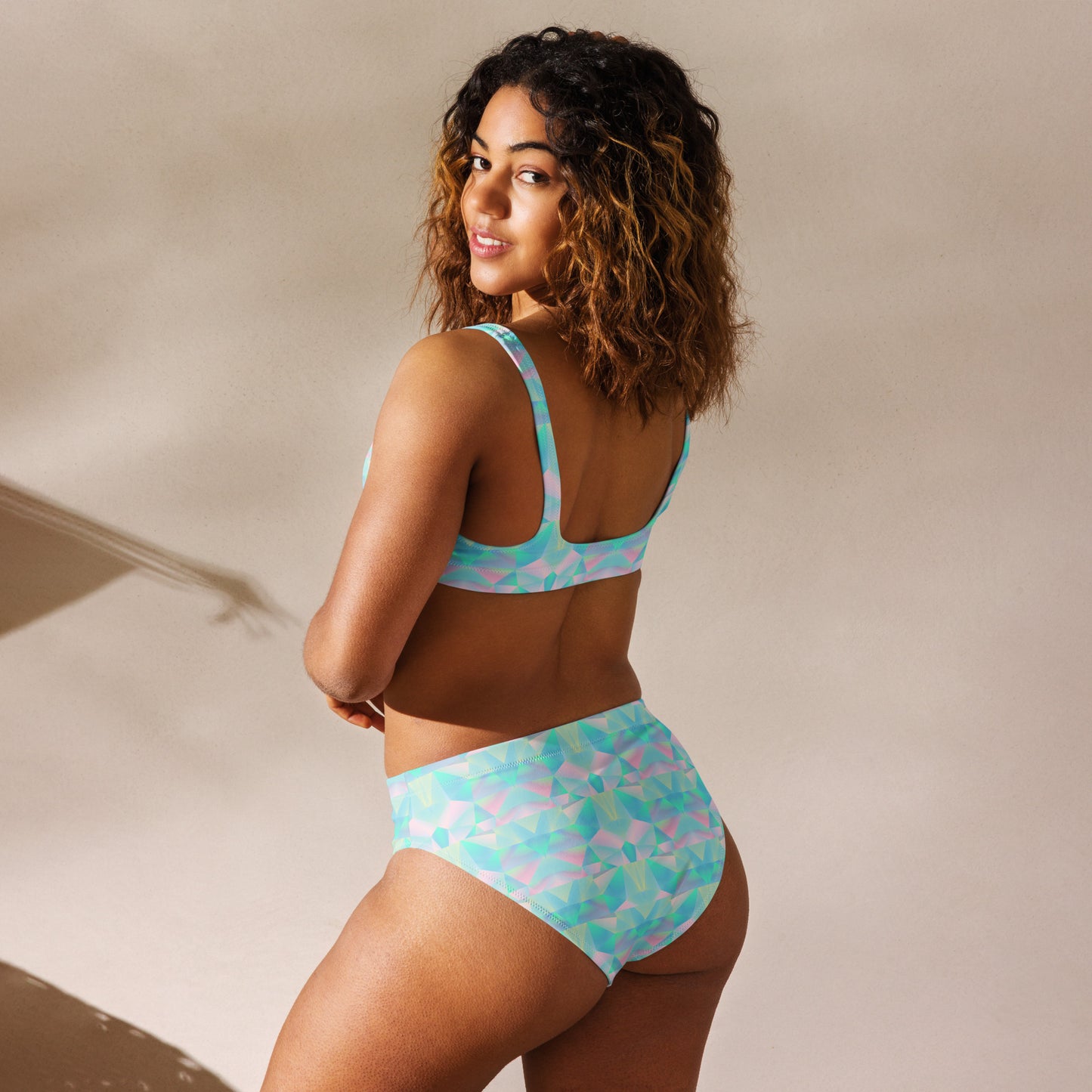 Image: This high waist two piece bathing suit features a pastel prism pattern in soft shades of teal, blue, and pink, creating a dreamy geometric design. Made from recycled materials, this swimsuit offers both style and sustainability. The high-waisted bottom provides comfort and coverage, while the top ensures support, making it a perfect choice for poolside lounging, tropical vacations, or beach outings, by jaecrece.