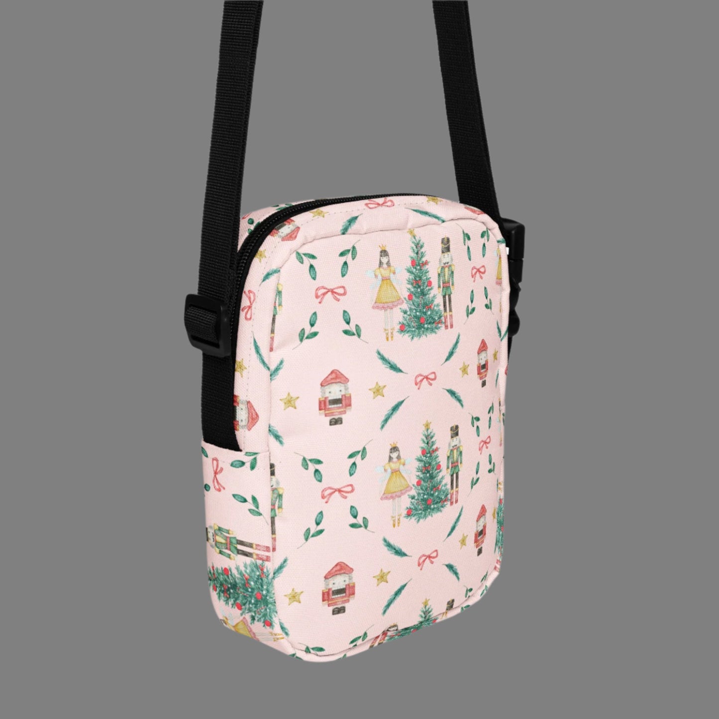 Image: Pink Coquette Nutcracker Utility Crossbody bag. The front of this small mini tote has a Christmas tree, Nutcracker, Sugarplum Fairy, Rocking Horse and a holiday present The rest of the purse is covered in a pattern of ribbons, garland, and Nutcrackers. May be worn across the waist/ hips, across the chest or as a mini backpack, by jaecrece
