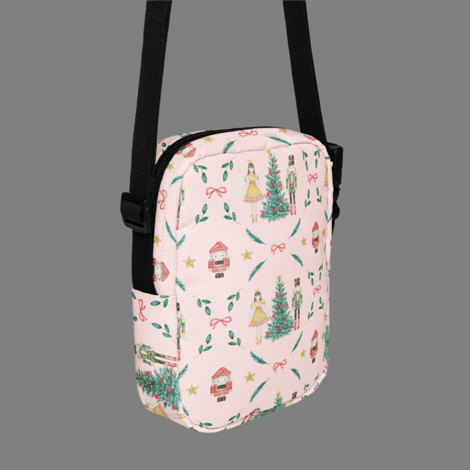 Image: Pink Coquette Nutcracker Utility Crossbody bag. The front of this small mini tote has a Christmas tree, Nutcracker, Sugarplum Fairy, Rocking Horse and a holiday present The rest of the purse is covered in a pattern of ribbons, garland, and Nutcrackers. May be worn across the waist/ hips, across the chest or as a mini backpack, by jaecrece
