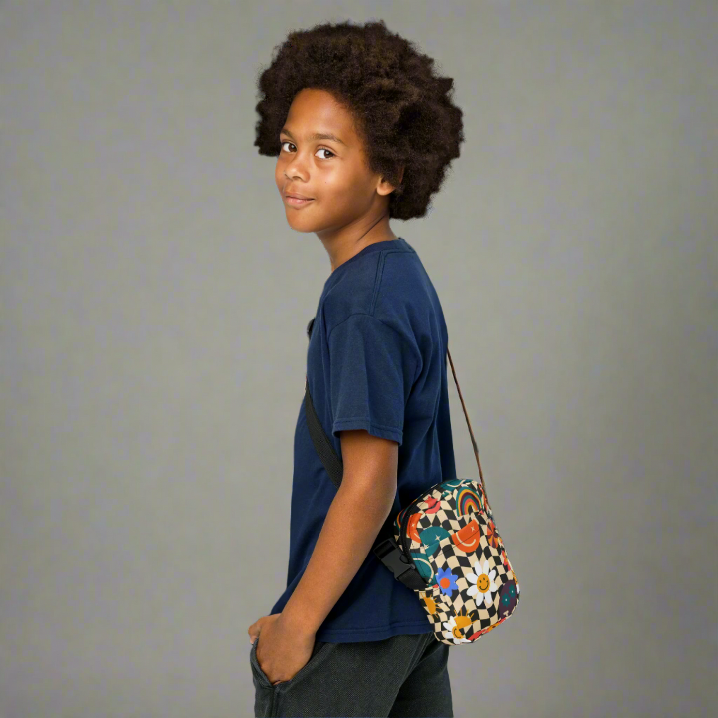Smiley Face Checkerboard Utility Crossbody Bag. This cute small canvas carryall is eco friendly, and features a black and khaki checkerboard background, with smiley face, rainbow and daisy graphics. It is perfect for hiking, vacations and festivals, and can be worn across the chest, or on the hips/ waist. By jaecrece.com