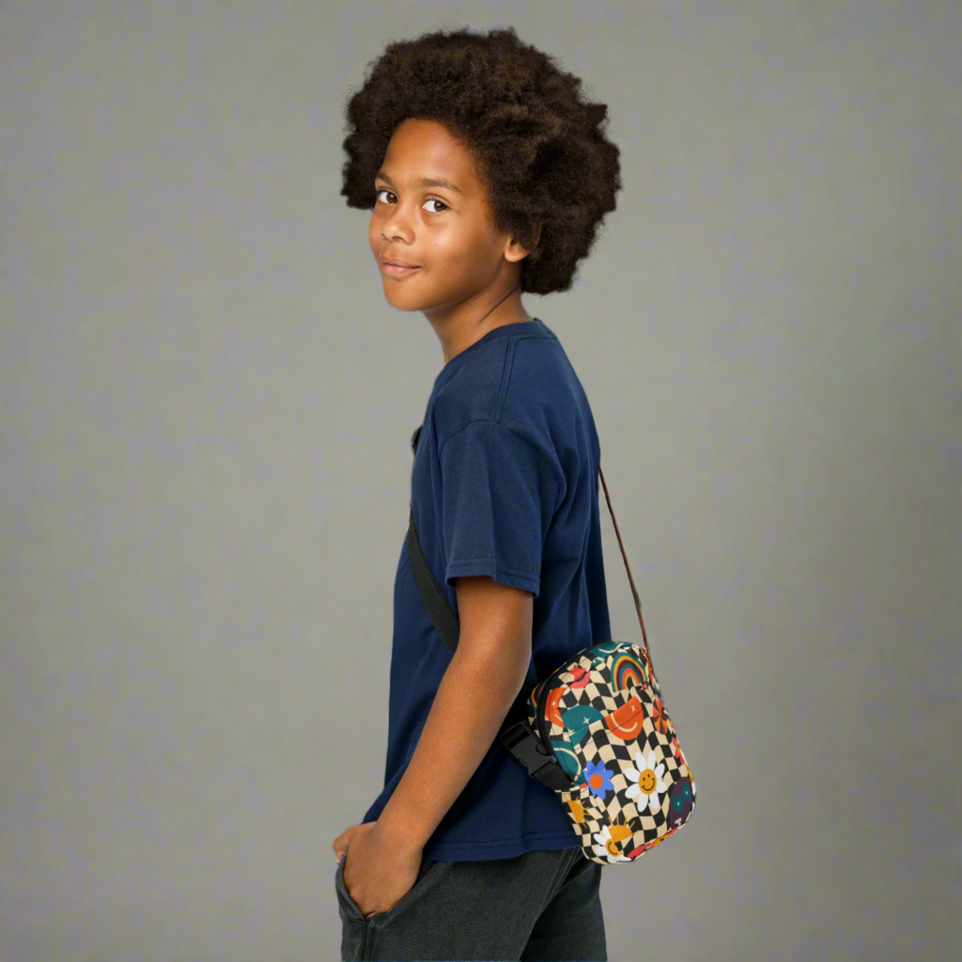 Smiley Face Checkerboard Utility Crossbody Bag. This cute small canvas carryall is eco friendly, and features a black and khaki checkerboard background, with smiley face, rainbow and daisy graphics. It is perfect for hiking, vacations and festivals, and can be worn across the chest, or on the hips/ waist. By jaecrece.com