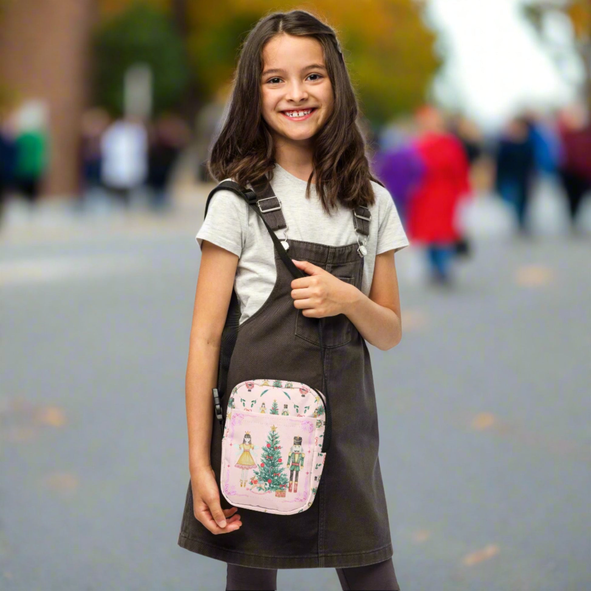 Image: Pink Coquette Nutcracker Utility Crossbody bag. The front of this small mini tote has a Christmas tree, Nutcracker, Sugarplum Fairy, Rocking Horse and a holiday present The rest of the purse is covered in a pattern of ribbons, garland, and Nutcrackers. May be worn across the waist/ hips, across the chest or as a mini backpack, by jaecrece