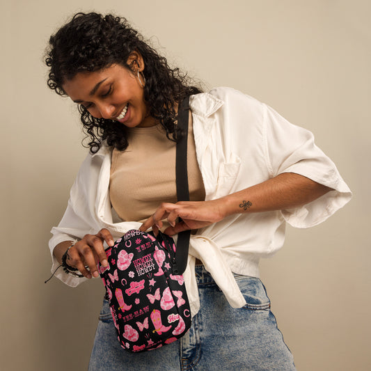 Image: Disco Cowgirl Canvas Crossbody Bag. This small black sling bag features a western glam hot pink pattern of cowgirl boots, cowgirl hats, butterflies and horseshoes. The pattern reads Disco Cowgirl, Yee-Haw and Howdy. The perfect mini backpack for bachelorette parties, gifts for teens or tweens, or trips to the state fair, by jaecrece