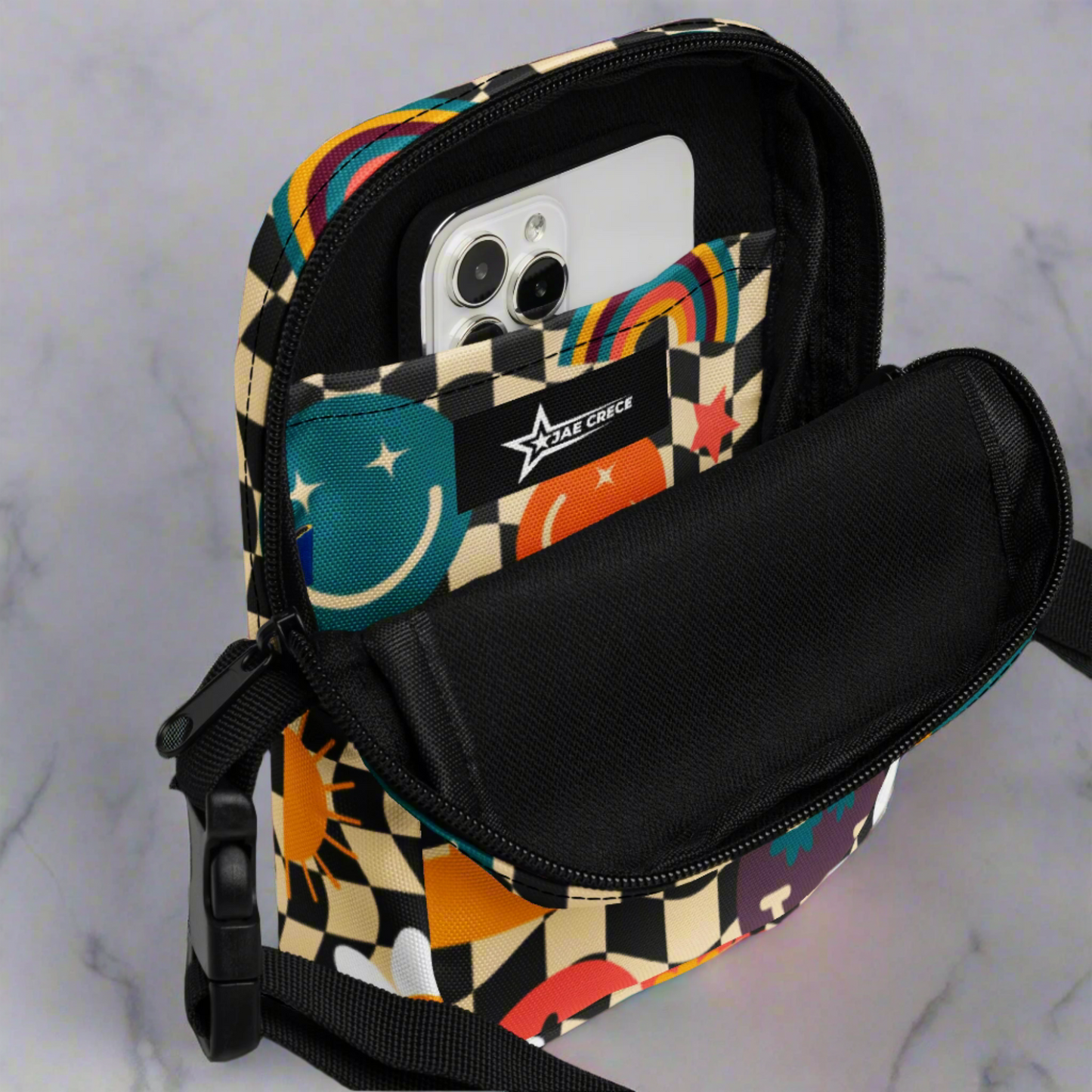 Smiley Face Checkerboard Utility Crossbody Bag. This cute small canvas carryall is eco friendly, and features a black and khaki checkerboard background, with smiley face, rainbow and daisy graphics. It is perfect for hiking, vacations and festivals, and can be worn across the chest, or on the hips/ waist. By jaecrece.com