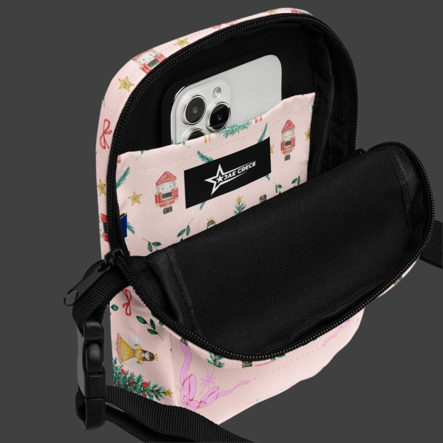 Image: Pink Coquette Nutcracker Utility Crossbody bag. The front of this small mini tote has a Christmas tree, Nutcracker, Sugarplum Fairy, Rocking Horse and a holiday present The rest of the purse is covered in a pattern of ribbons, garland, and Nutcrackers. May be worn across the waist/ hips, across the chest or as a mini backpack, by jaecrece