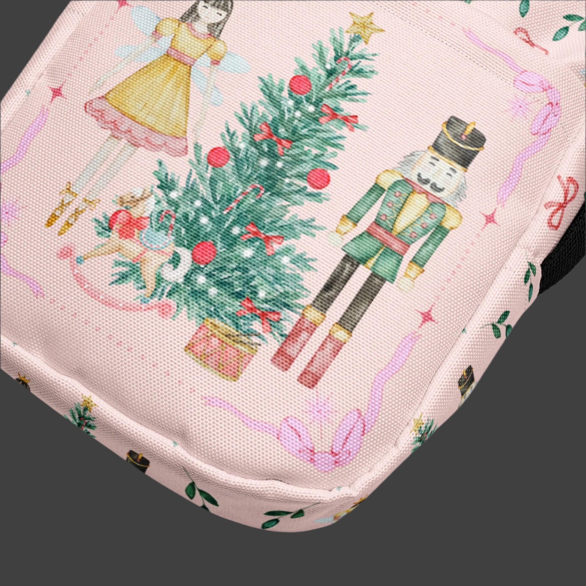 Image: Pink Coquette Nutcracker Utility Crossbody bag. The front of this small mini tote has a Christmas tree, Nutcracker, Sugarplum Fairy, Rocking Horse and a holiday present The rest of the purse is covered in a pattern of ribbons, garland, and Nutcrackers. May be worn across the waist/ hips, across the chest or as a mini backpack, by jaecrece