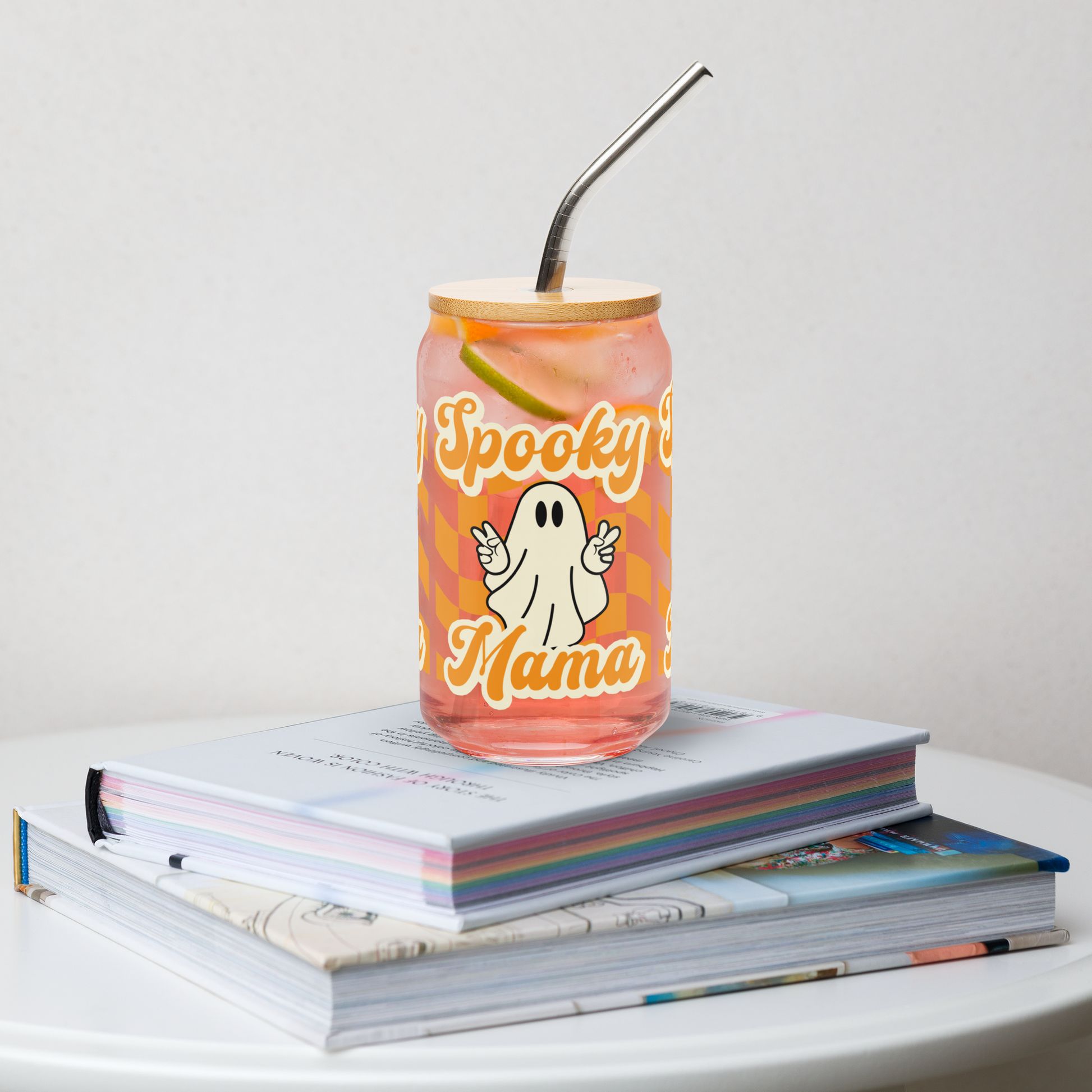Cute Ghost Halloween Fall 16 oz Sipper Glass Funny Halloween Gift for Mom Spooky Mama Halloween Glass Coffee Cup, featuring a orange checkerboard design with a white ghost giving the peace sign and the text Spooky Mama in orange and white cursive bubble font by jaecrece.com