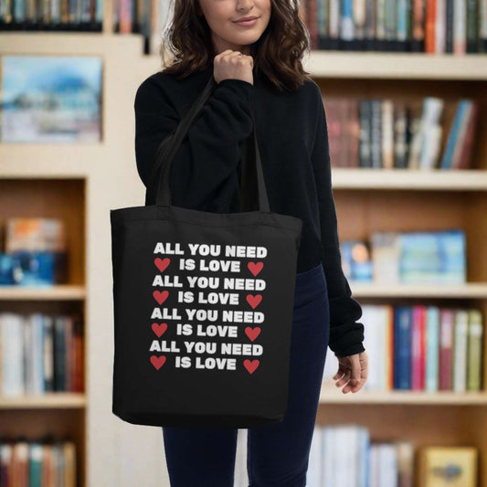 Reusable All You Need is Love tote bag made from 100% certified organic cotton, perfect for everyday errands, grocery shopping, or trips to the library. This durable canvas tote features double-sided printing and long shoulder straps, making it a practical and eco-conscious gift for teachers, moms, students, or anyone who values sustainability and minimalist design in their daily routine.