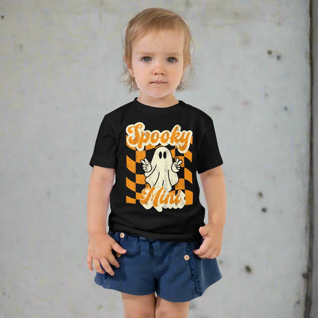 Spooky Mini Halloween Toddler Shirt, featuring a orange checkerboard pattern with a cute ghost graphic. The text reads Spooky Mini, by jaecrece