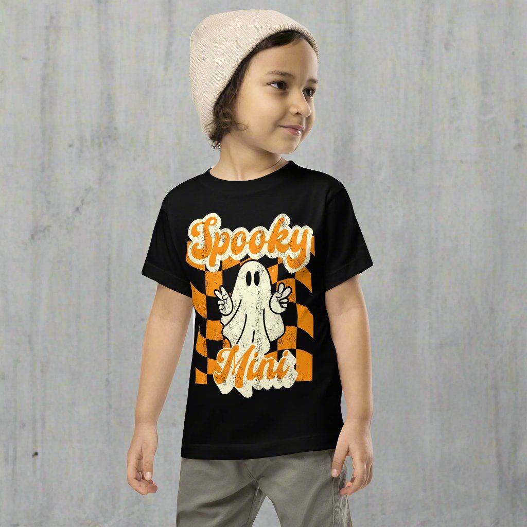 Spooky Mini Halloween Toddler Shirt, featuring a orange checkerboard pattern with a cute ghost graphic. The text reads Spooky Mini, by jaecrece