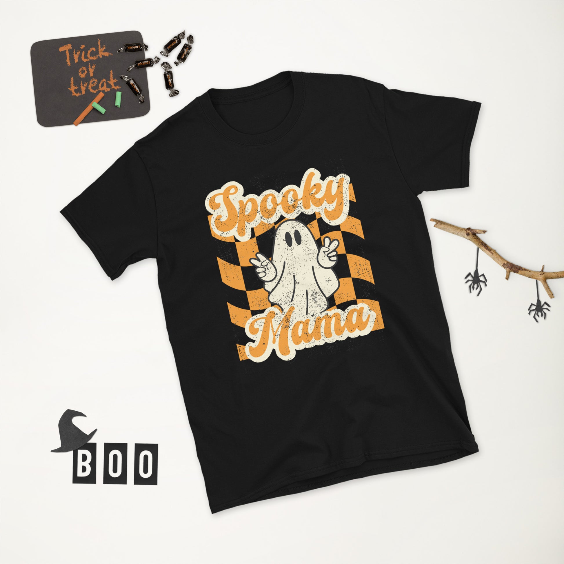 Spooky Mama Halloween Tshirt, featuring a orange checkerboard design with a white ghost giving the peace sign, and the text "Spooky Mama" in orange and white cursive bubble font, by jaecrece.com