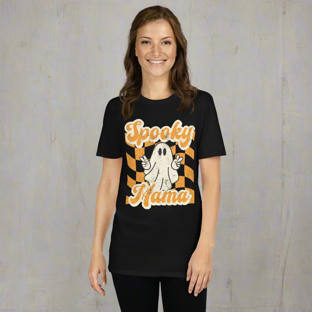 Spooky Mama Halloween Tshirt, featuring a orange checkerboard design with a white ghost giving the peace sign, and the text "Spooky Mama" in orange and white cursive bubble font, by jaecrece.com