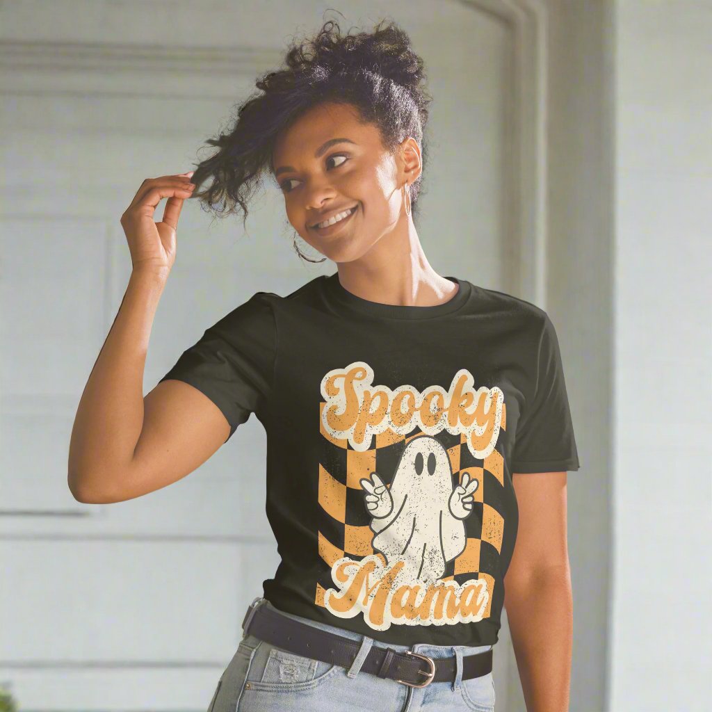 Spooky Mama Halloween Tshirt, featuring a orange checkerboard design with a white ghost giving the peace sign, and the text "Spooky Mama" in orange and white cursive bubble font, by jaecrece.com