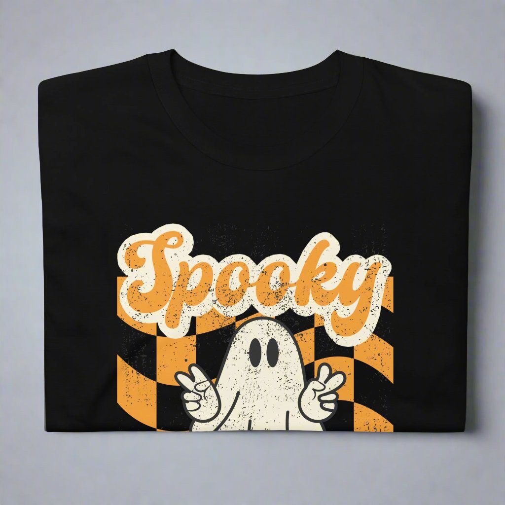 Spooky Mama Halloween Tshirt, featuring a orange checkerboard design with a white ghost giving the peace sign, and the text "Spooky Mama" in orange and white cursive bubble font, by jaecrece.com
