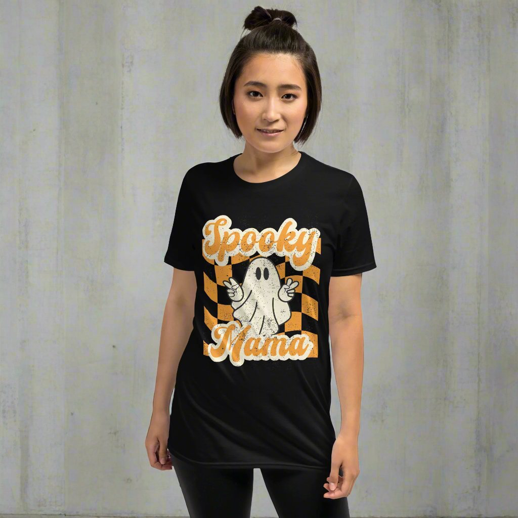 Spooky Mama Halloween Tshirt, featuring a orange checkerboard design with a white ghost giving the peace sign, and the text "Spooky Mama" in orange and white cursive bubble font, by jaecrece.com