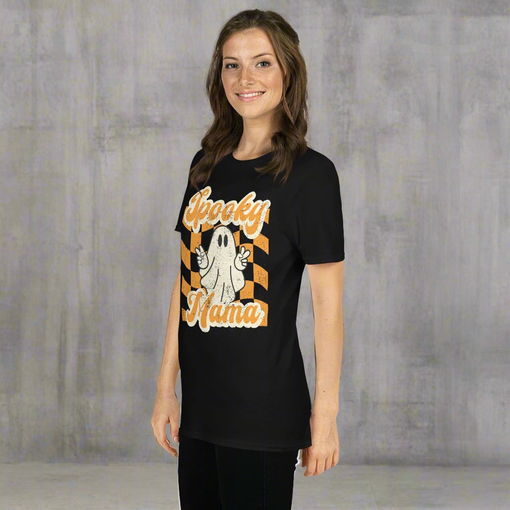 Spooky Mama Halloween Tshirt, featuring a orange checkerboard design with a white ghost giving the peace sign, and the text "Spooky Mama" in orange and white cursive bubble font, by jaecrece.com