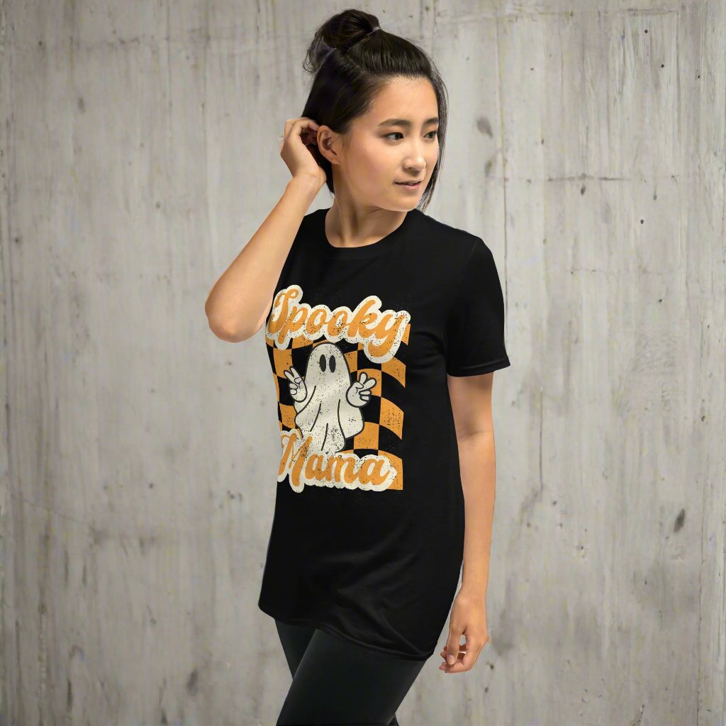 Spooky Mama Halloween Tshirt, featuring a orange checkerboard design with a white ghost giving the peace sign, and the text "Spooky Mama" in orange and white cursive bubble font, by jaecrece.com