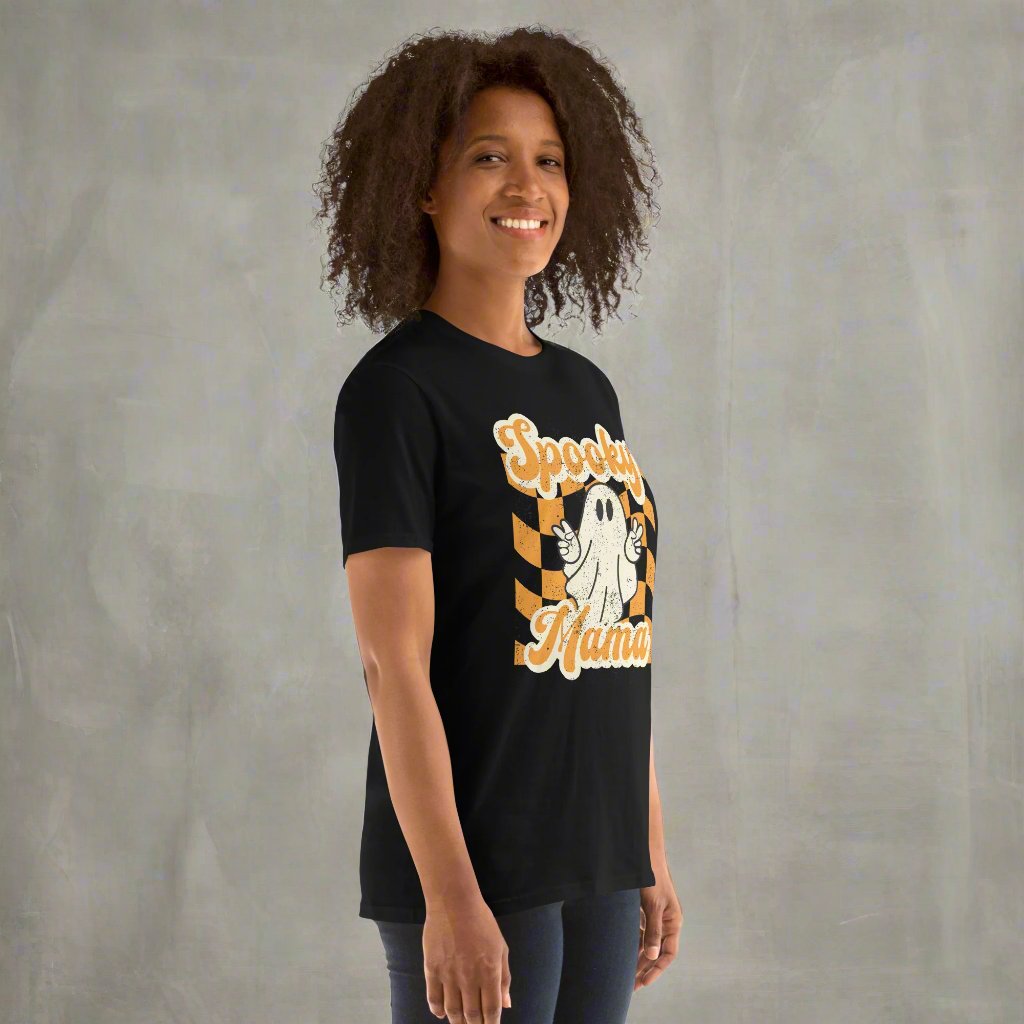 Spooky Mama Halloween Tshirt, featuring a orange checkerboard design with a white ghost giving the peace sign, and the text "Spooky Mama" in orange and white cursive bubble font, by jaecrece.com