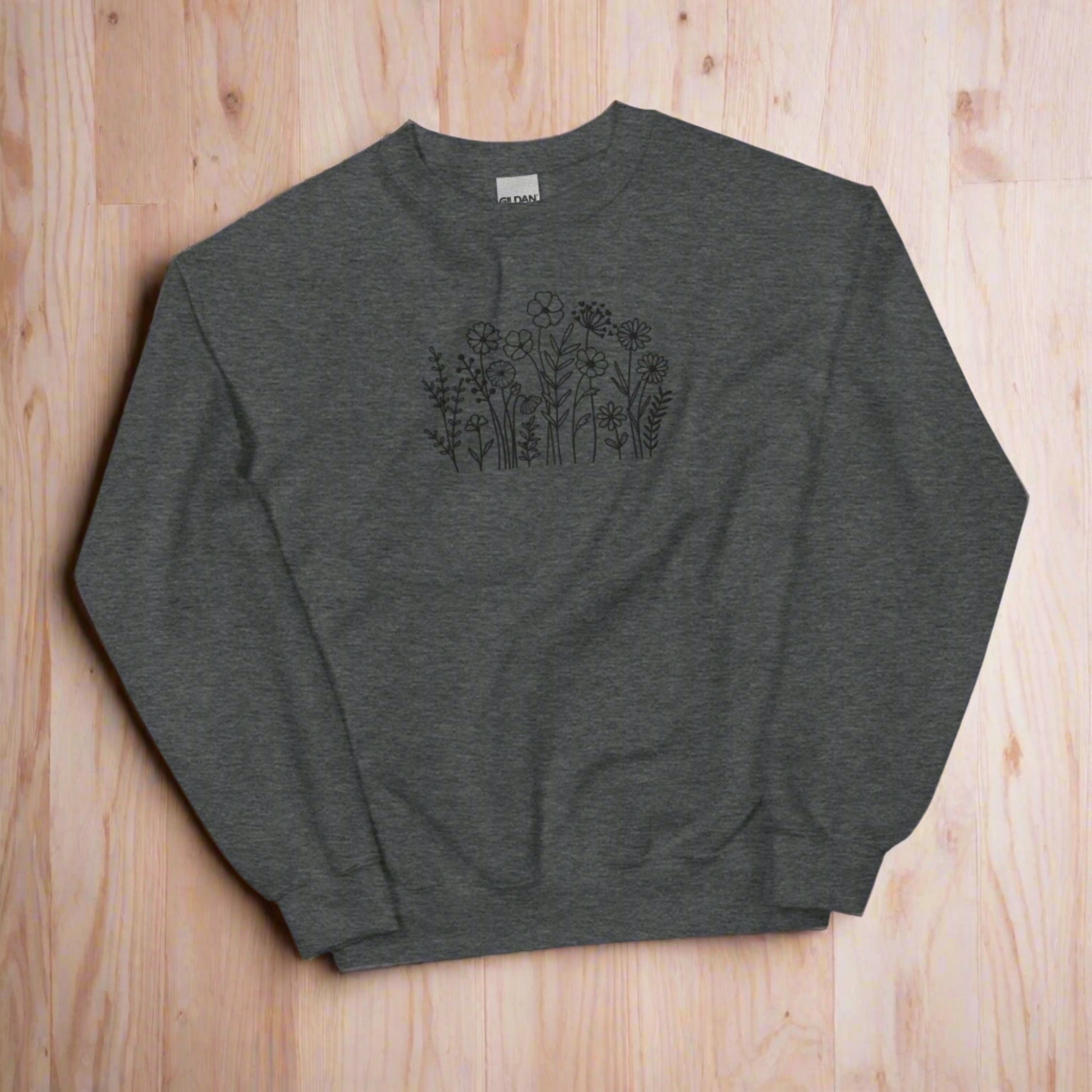 Image: A cozy dark grey sweatshirt with delicate black wildflower embroidery across the chest, showcasing a minimalist yet elegant botanical design. The soft fabric drapes effortlessly, offering comfort for everyday wear. This floral nature crewneck is perfect for layering, adding a subtle floral charm to casual outfits. A thoughtful gift for plant lovers or those who appreciate nature-inspired fashion, by jaecrece.