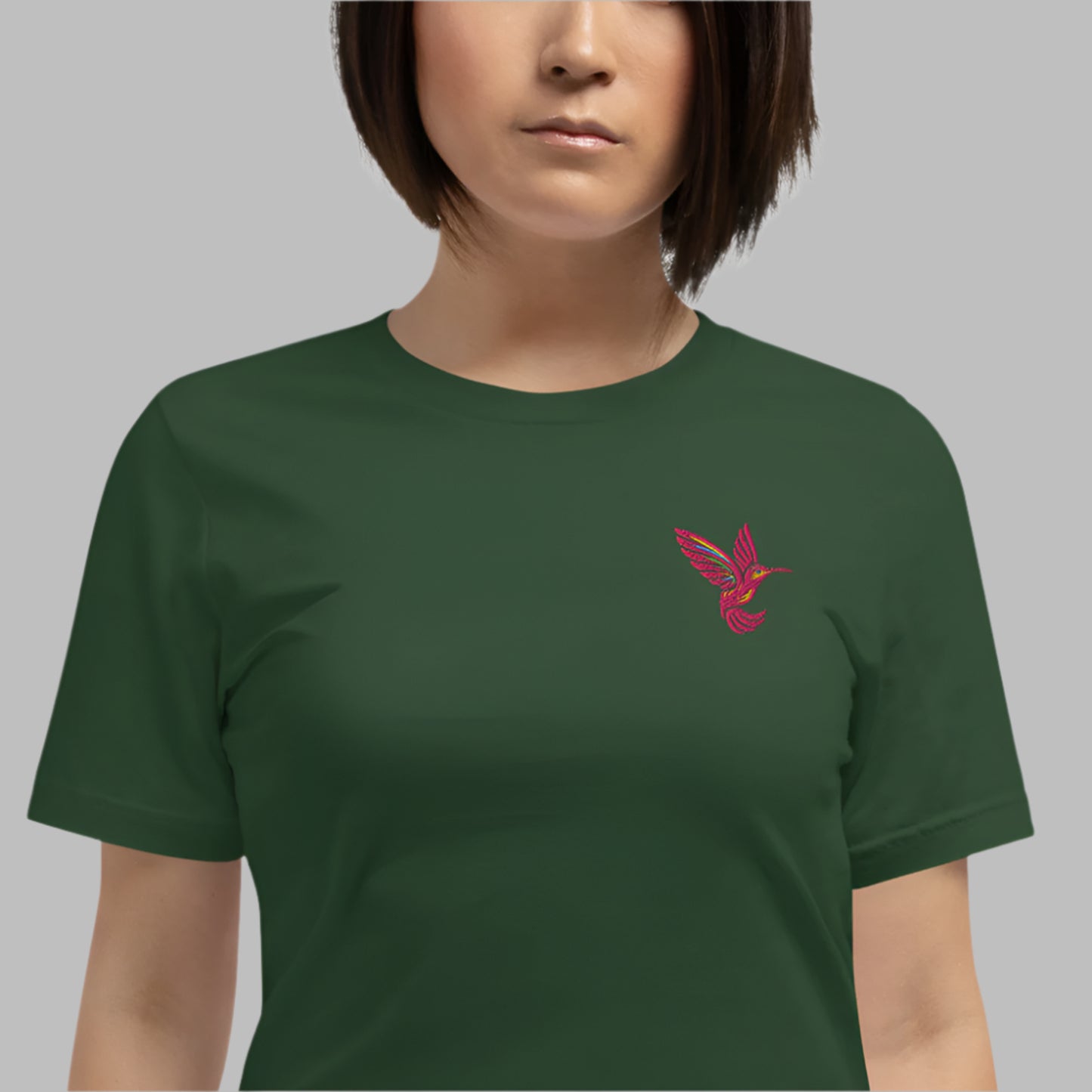 Model wearing a forest green embroidered shirt with a pink hummingbird stitched on the chest. This lightweight cotton tee is perfect for nature lovers and fans of slow fashion. With a pre-shrunk fit and breathable fabric, this unisex shirt in sizes XS–5XL makes a great gift for bird lovers, eco-conscious shoppers, and those who love embroidered t-shirts.