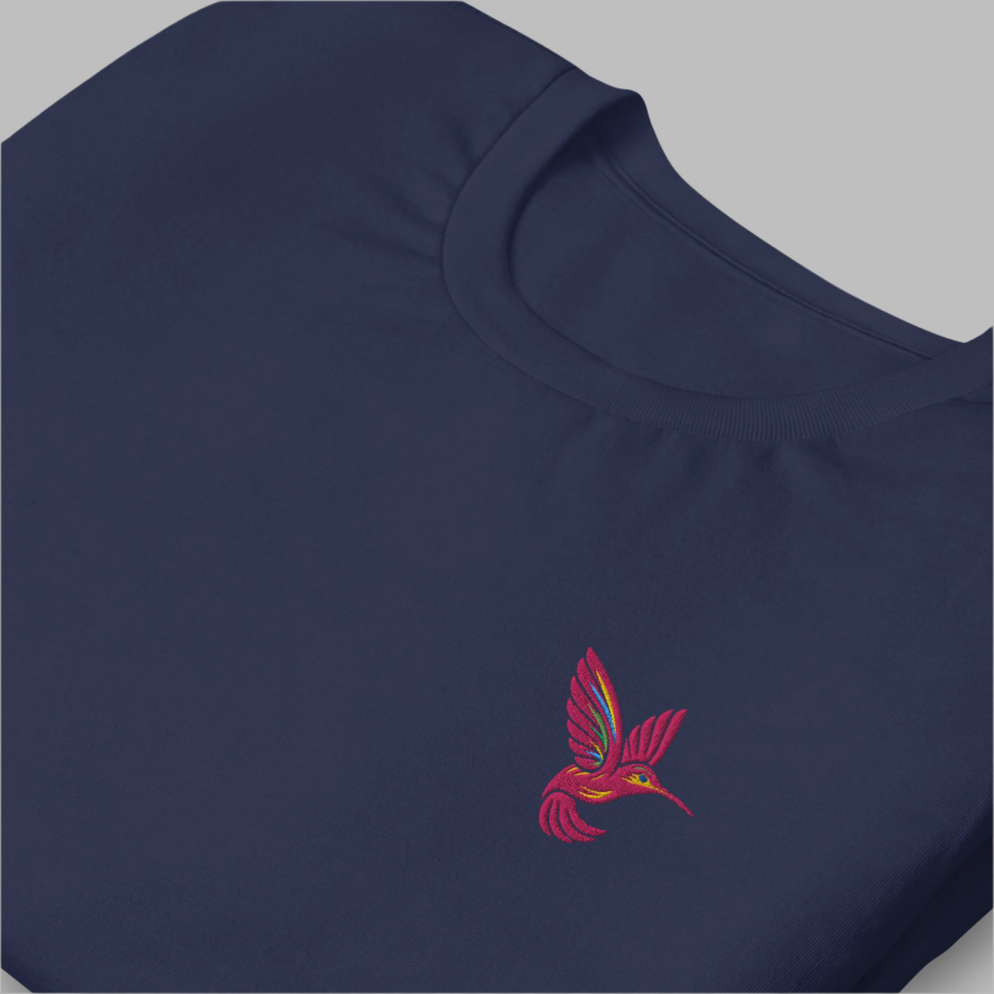 Flat lay of a navy blue embroidered hummingbird t-shirt, made with soft combed and ring-spun cotton. Featuring a small pink hummingbird design on the front chest, this shirt offers a minimalist take on nature-inspired fashion. Great for everyday wear, bird-themed gifts, or slow fashion shoppers seeking unique embroidered clothing in inclusive sizing XS–5XL.