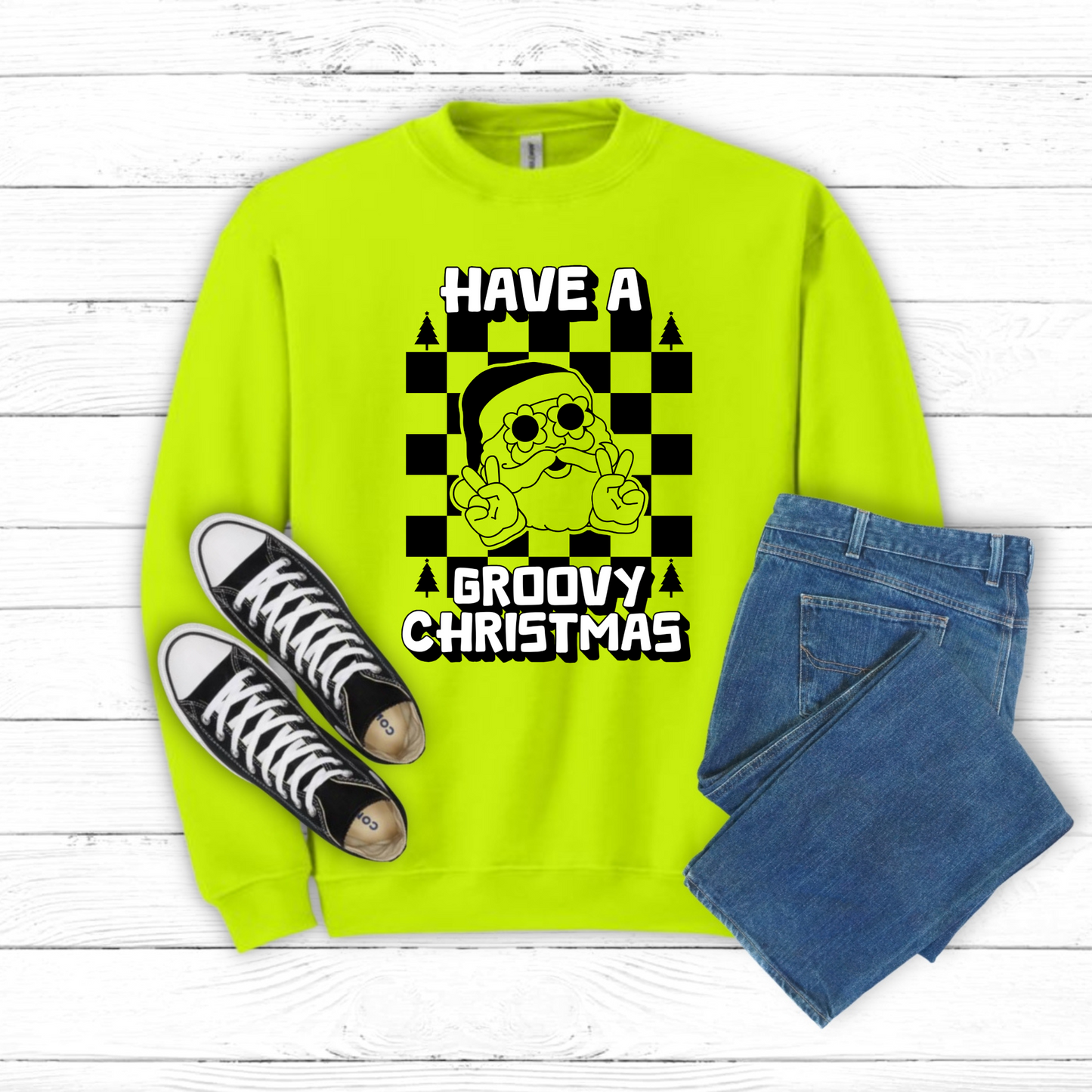 Image: retro Santa christmas sweatshirt available in pink and bright green. The text reads Have a groovy Christmas, with a black checkerboard background, and a vintage Santa wearing daisy sunglasses and giving the peace sign. The perfect gift for those who love a funky vintage aesthetic, by jaecrece