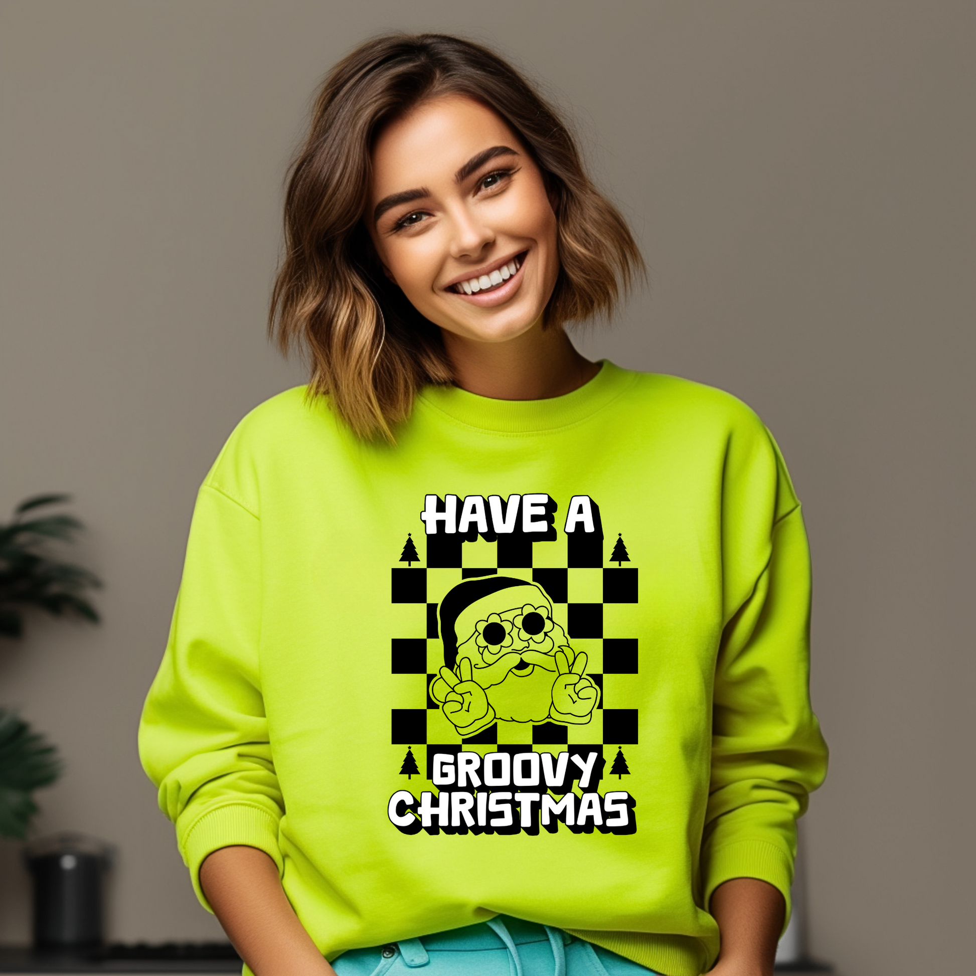 Image: retro Santa christmas sweatshirt available in pink and bright green. The text reads Have a groovy Christmas, with a black checkerboard background, and a vintage Santa wearing daisy sunglasses and giving the peace sign. The perfect gift for those who love a funky vintage aesthetic, by jaecrece