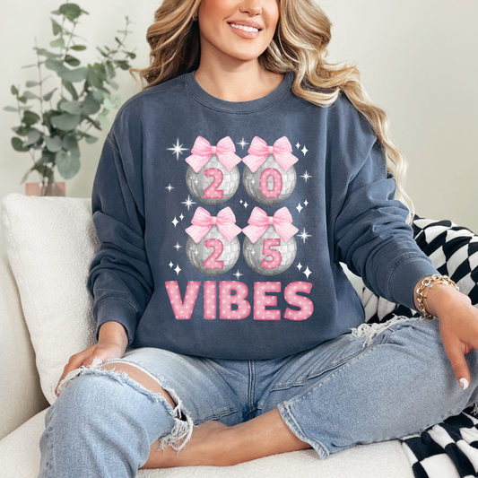 Image: Happy New Years Eve Sweatshirt is available in four colors- denim, graphite, white and chalky mint. There are 4 silver disco balls, with  pink gingham ribbon and 2025 on each. VIBES is in pink coquette polka dot block letters. by jaecrece