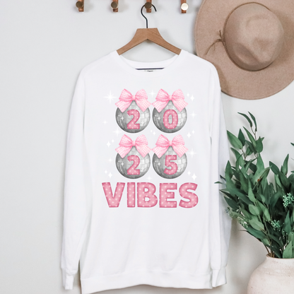 Image: Happy New Years Eve Sweatshirt is available in four colors- denim, graphite, white and chalky mint. There are 4 silver disco balls, with  pink gingham ribbon and 2025 on each. VIBES is in pink coquette polka dot block letters. by jaecrece