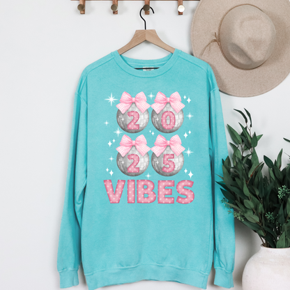 Image: Happy New Years Eve Sweatshirt is available in four colors- denim, graphite, white and chalky mint. There are 4 silver disco balls, with  pink gingham ribbon and 2025 on each. VIBES is in pink coquette polka dot block letters. by jaecrece