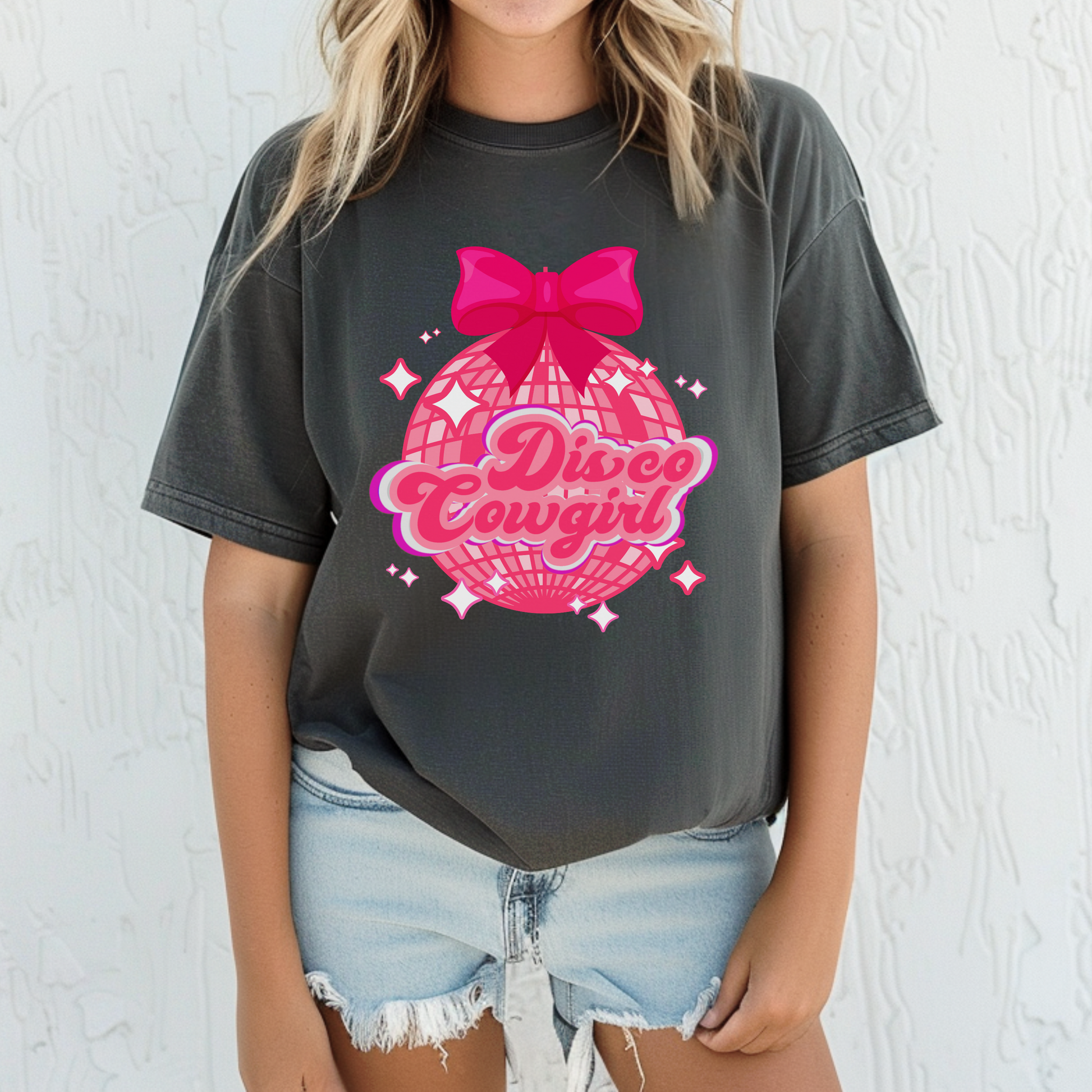 Pink disco ball graphic with coquette bow shines on this women’s Disco Cowgirl Comfort Colors tee, perfect for western-themed parties, girls’ weekends, and Nashville adventures. Featuring a fun design with pink and purple script and star details, this soft tee offers an oversized vintage fit. Ideal for country concert outfits or cute bachelorette groups. Sizes S–4XL.